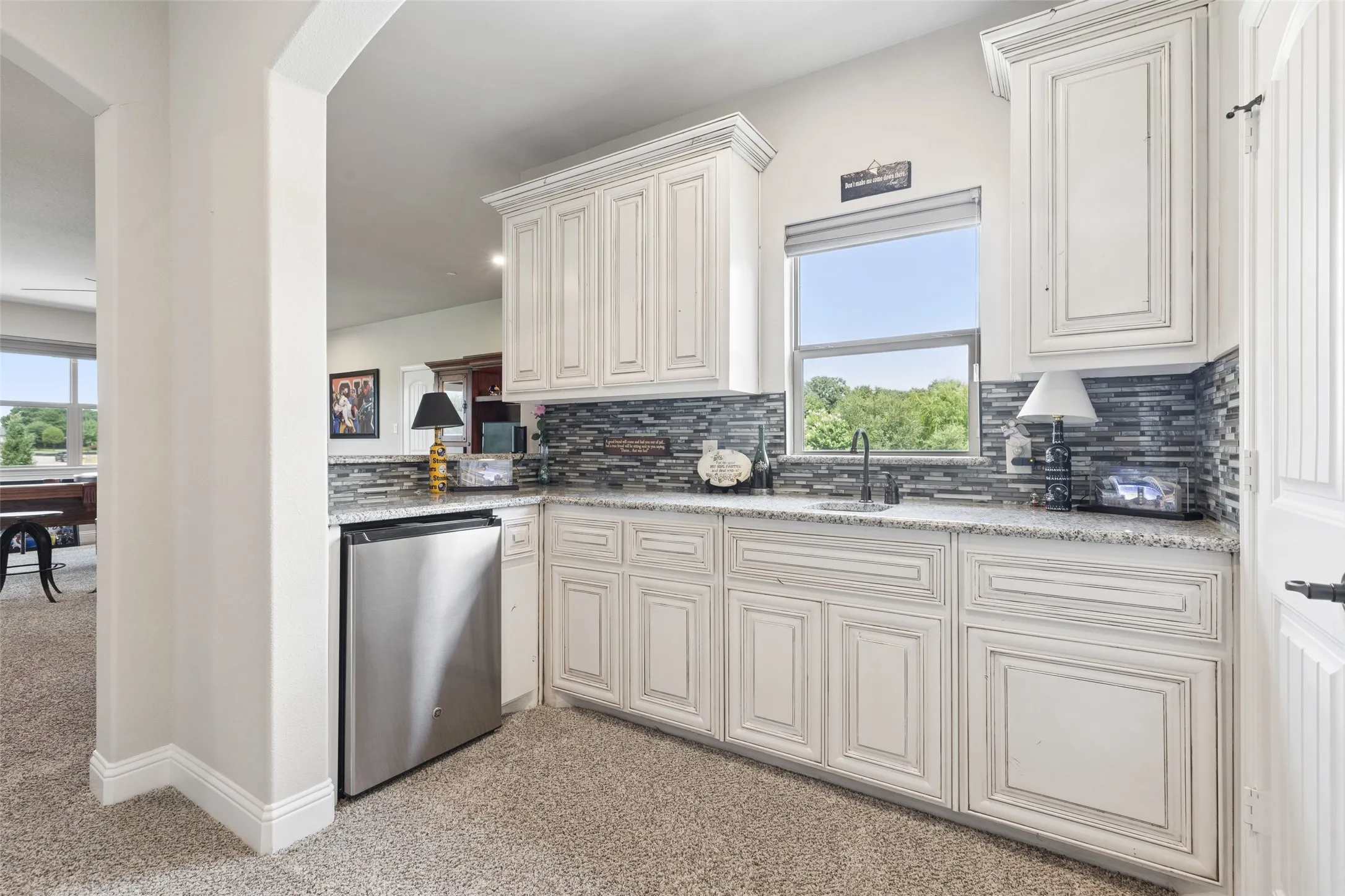 Built-in wet bar featuring white cabinetry, a stainless steel undercounter refrigerator, a tile backsplash, and a sink with a black faucet