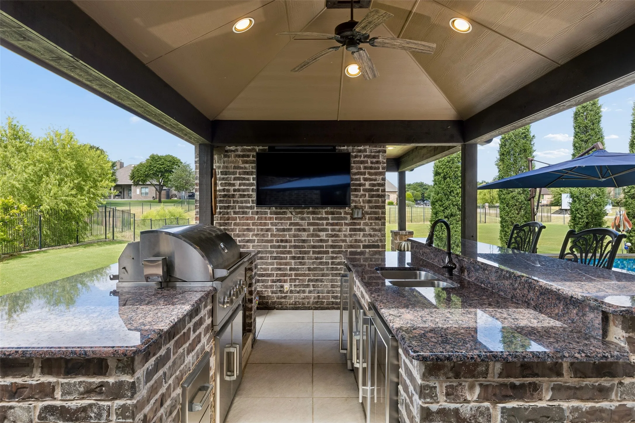 Expansive outdoor kitchen featuring a built-in stainless steel grill, integrated sink, and granite countertops