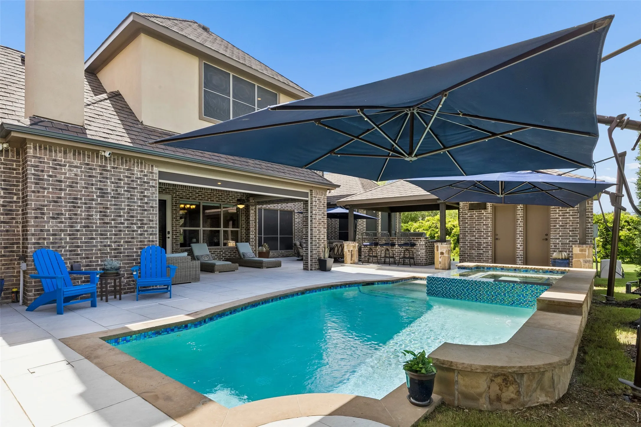 Resort-style backyard featuring a swimming pool with integrated spa, expansive patio with covered lounge area, and a built-in outdoor bar