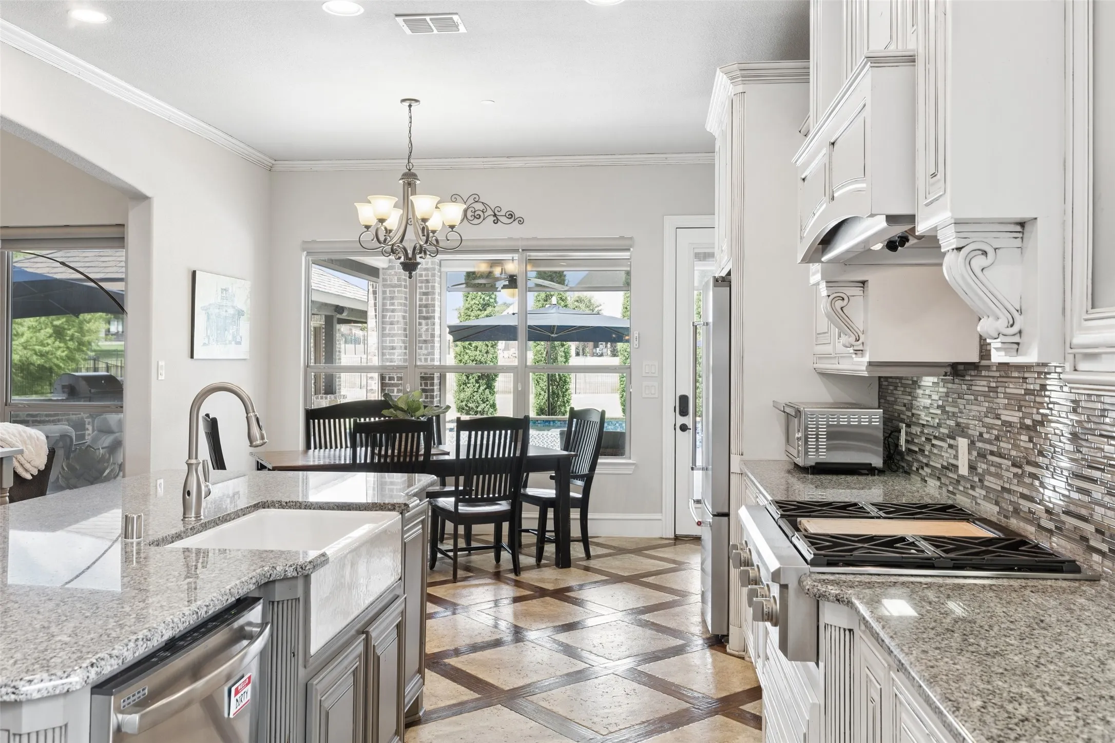 Kitchen featuring grey cabinetry, granite countertops, a farmhouse sink, stainless steel appliances, and a mosaic tile backsplash