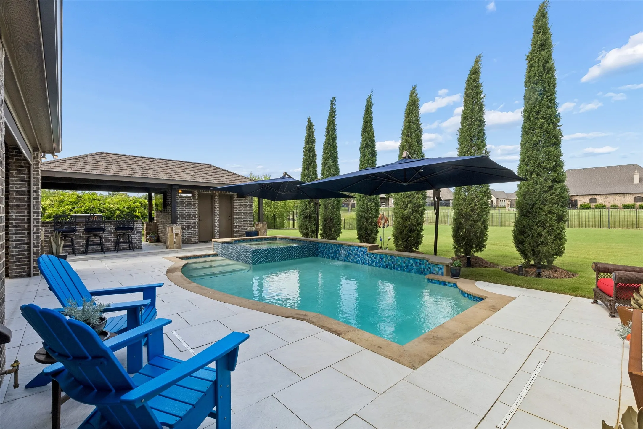 Backyard oasis featuring a curvilinear pool with integrated spa, an expansive paved patio, and a covered outdoor kitchen with a bar