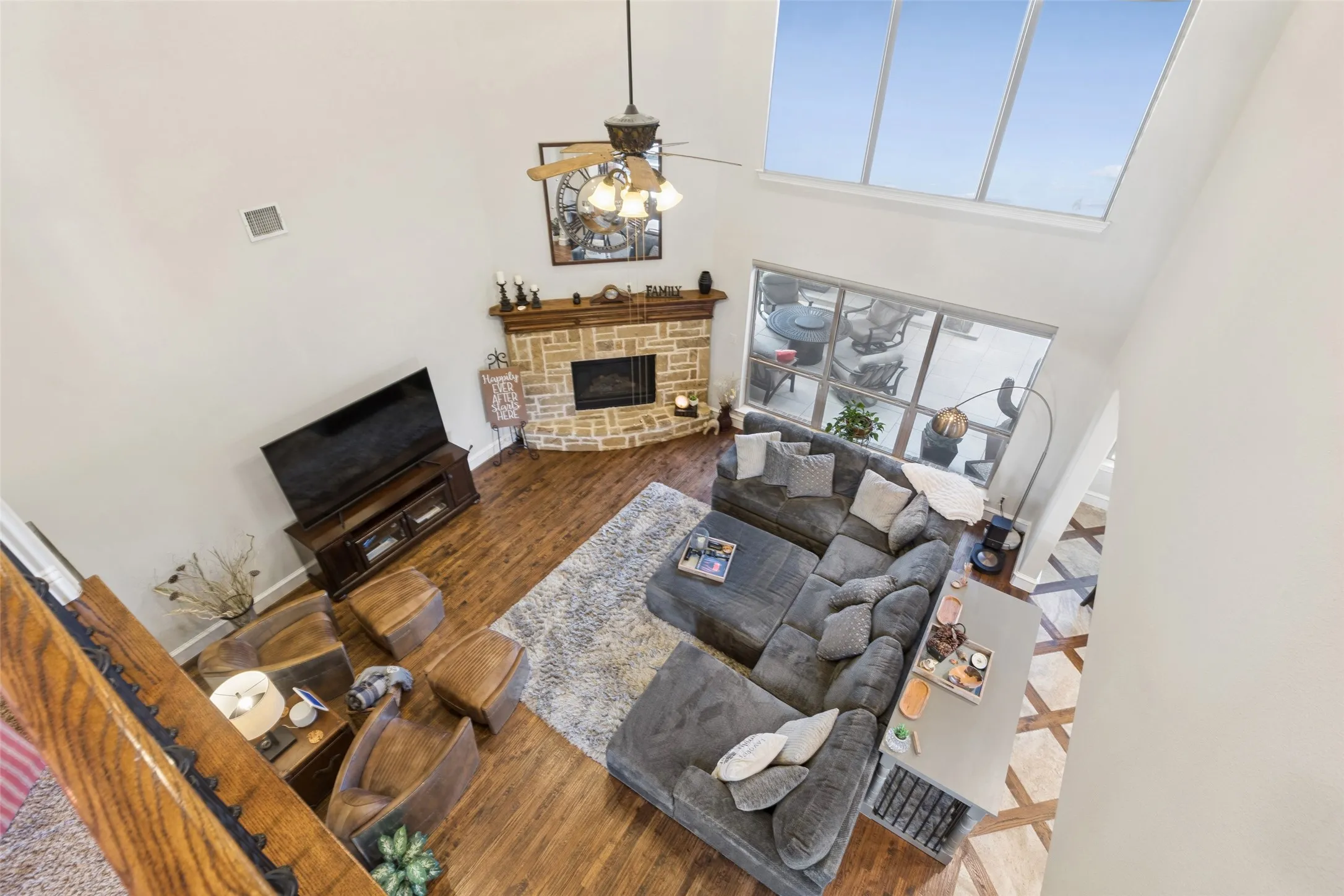 Two-story living area featuring a stone-faced fireplace with wood mantel, wood-finish flooring, and a ceiling fan