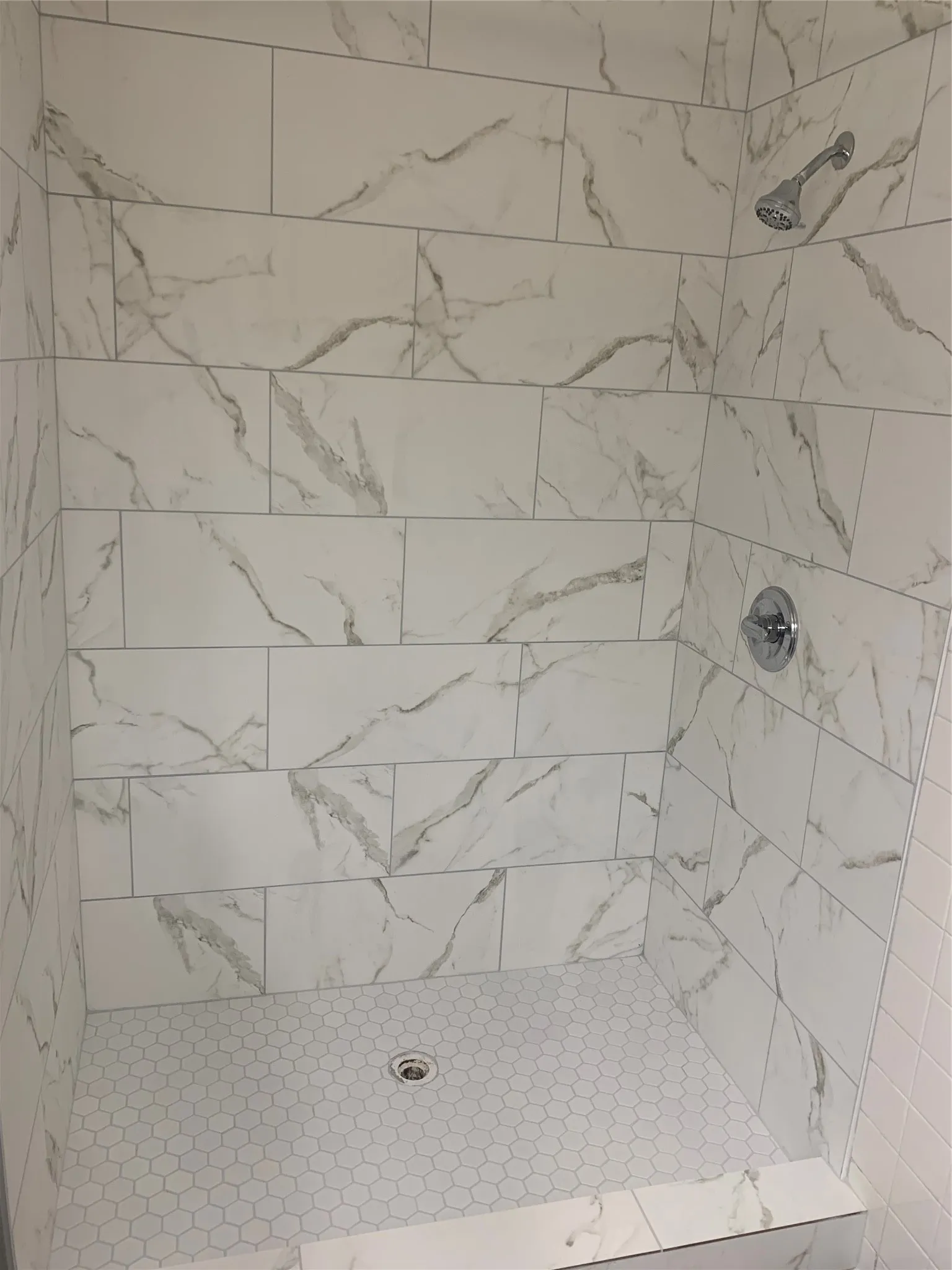 Shower stall featuring large format white tile with gray veining, chrome shower head, and coordinating chrome fixtures