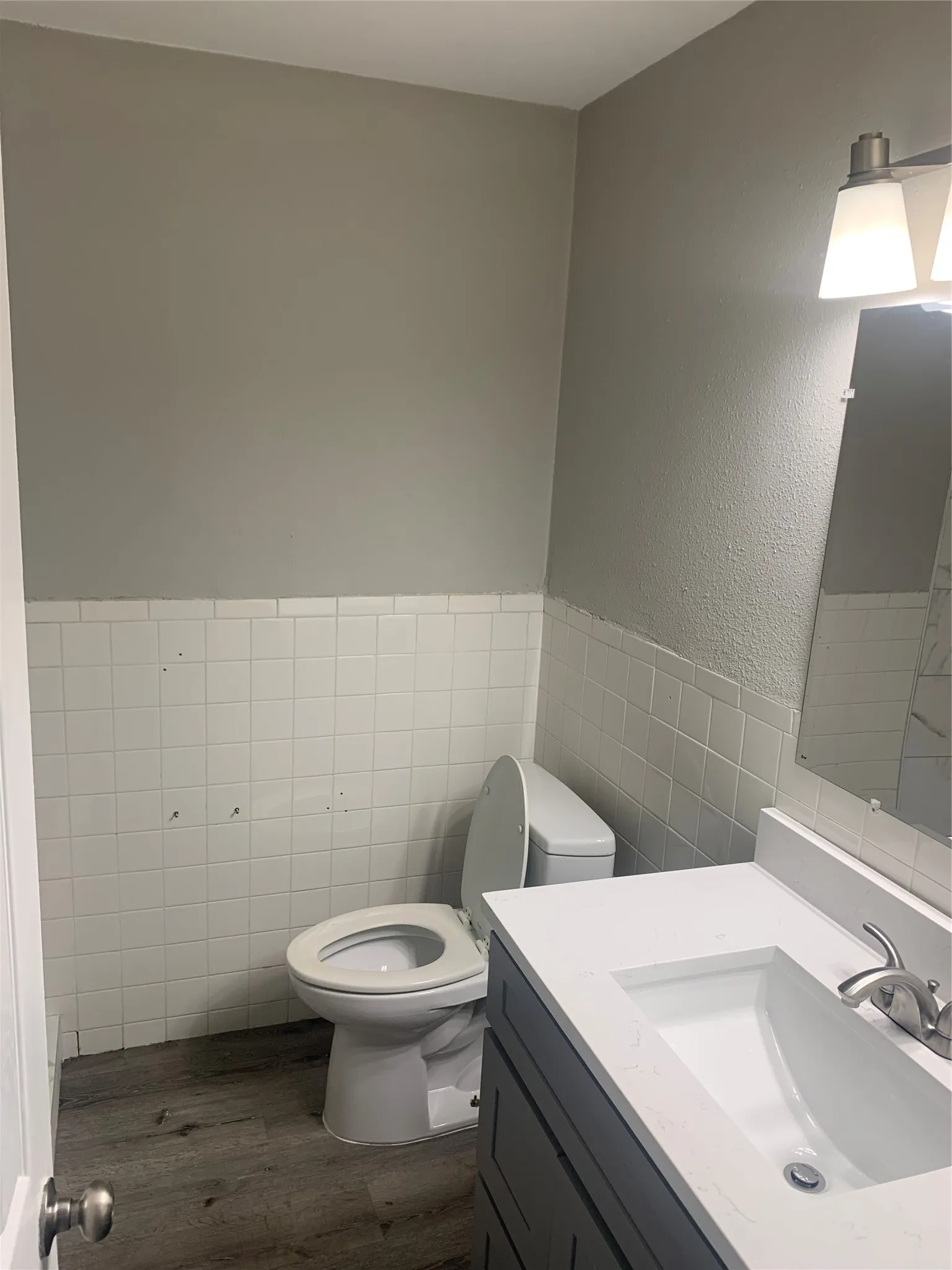 Bathroom featuring a white vanity with an integrated sink, a two-bulb sconce, a mirror, and wood-finish flooring