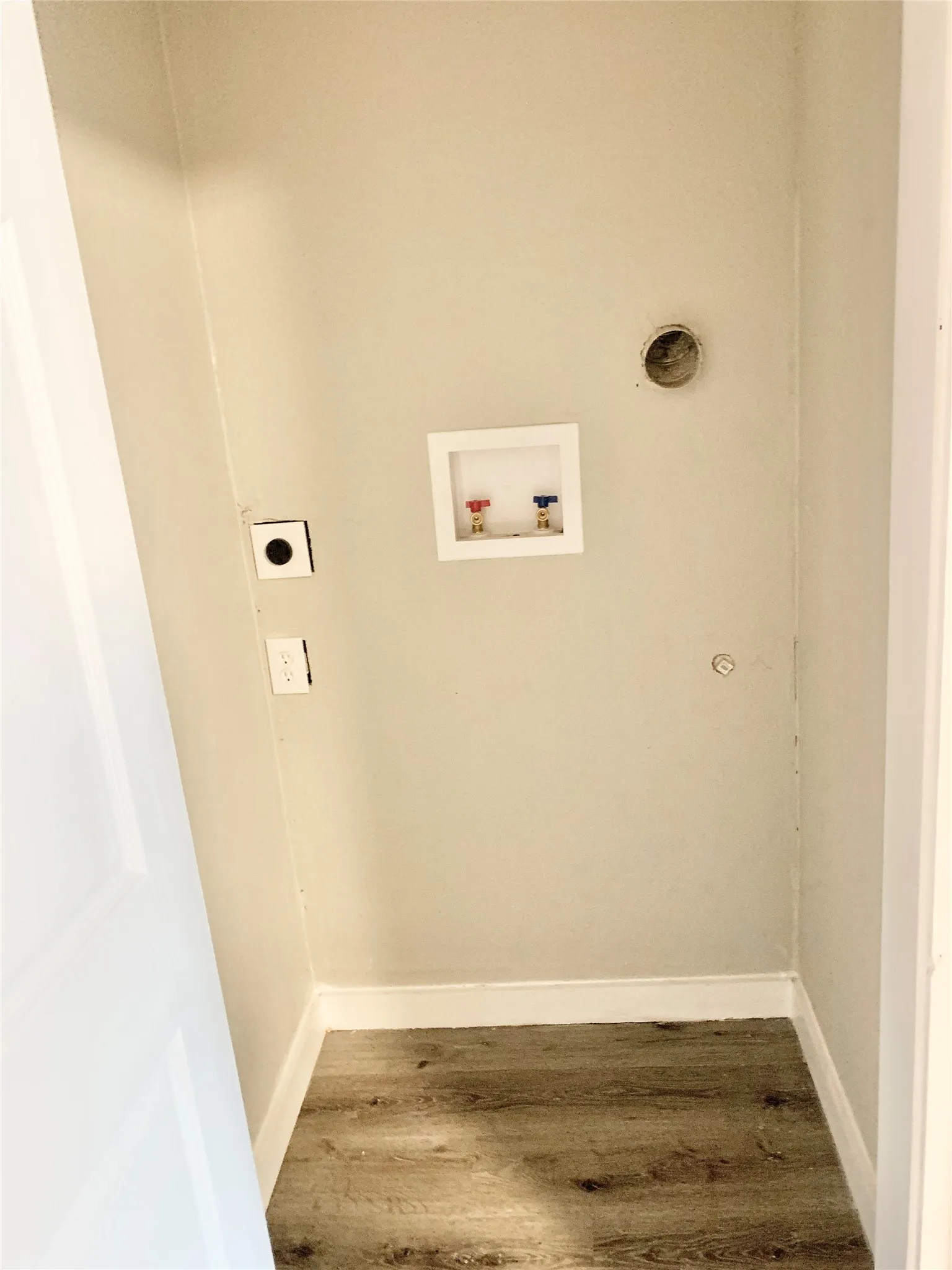 Dedicated utility space featuring wood-finish flooring, light neutral wall paint, and white baseboards