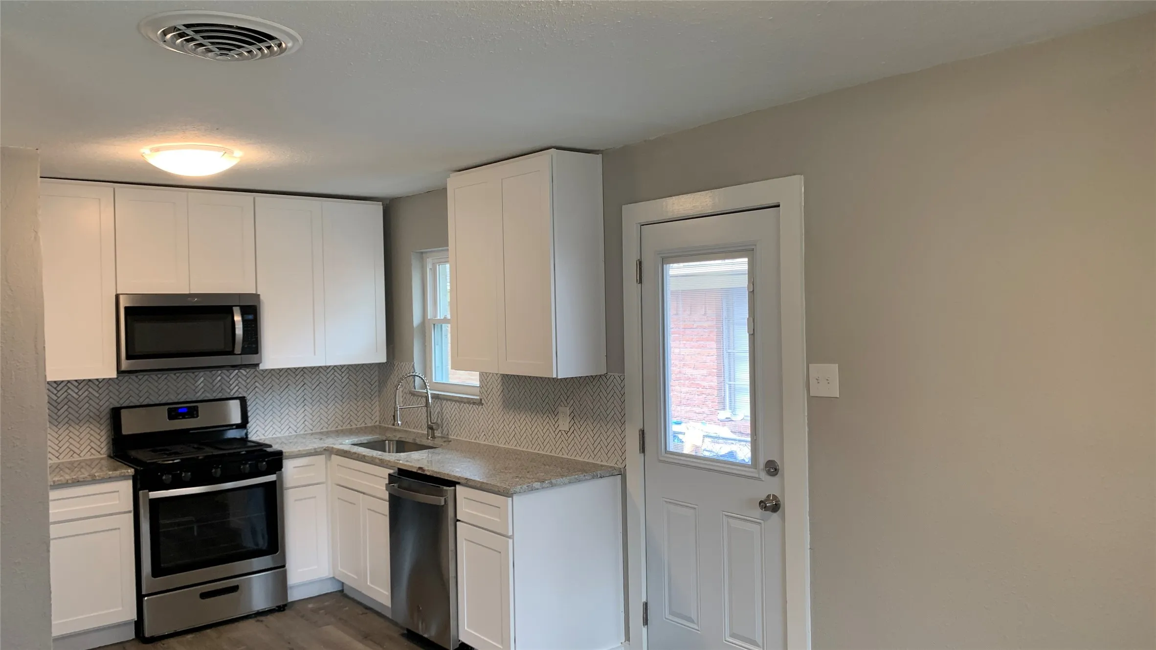 Kitchen featuring white cabinetry, stainless steel appliances, granite countertops, and a herringbone tile backsplash