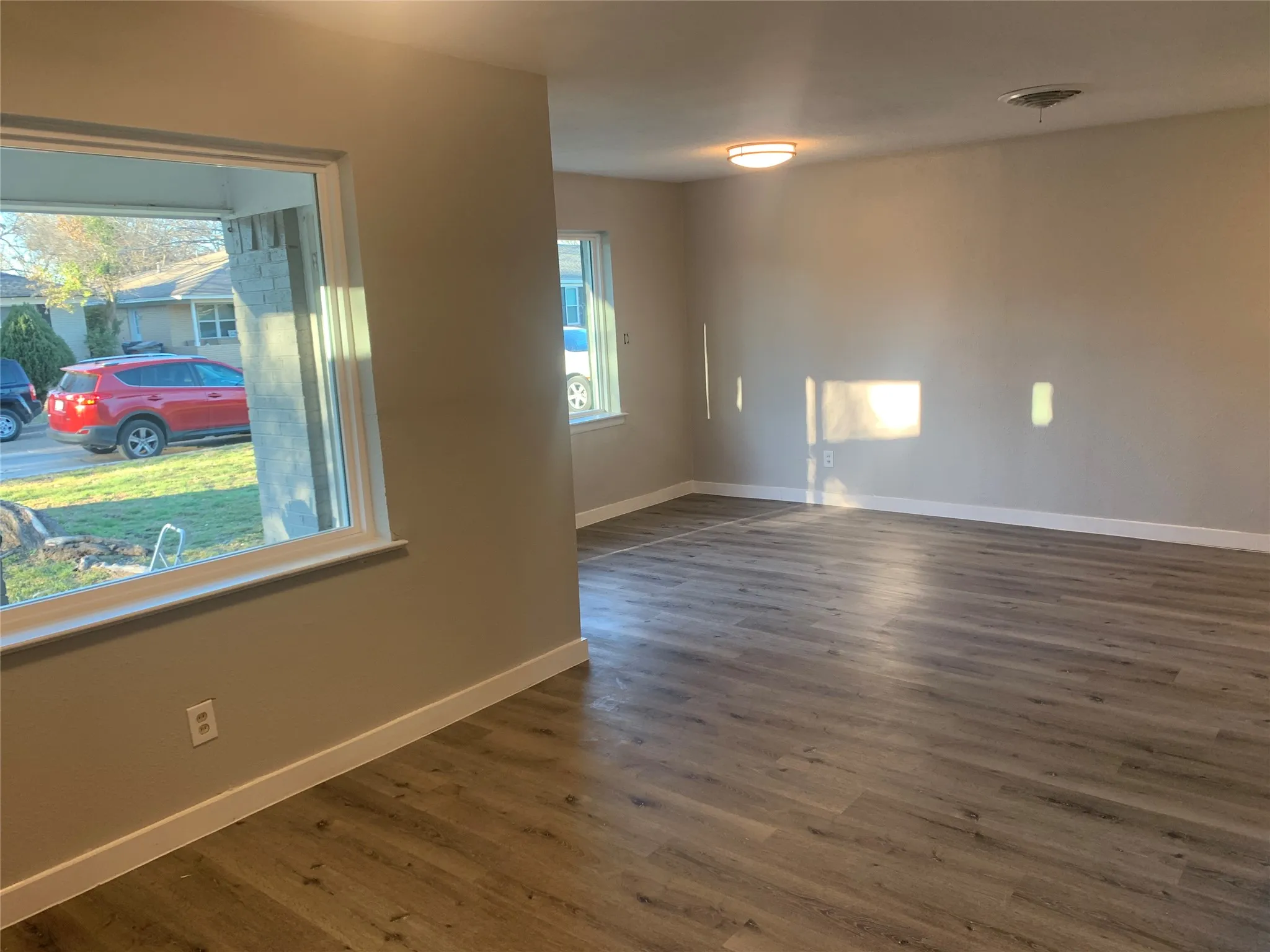 Spacious room featuring wood-finish flooring, neutral wall tones, white baseboards, and multiple windows