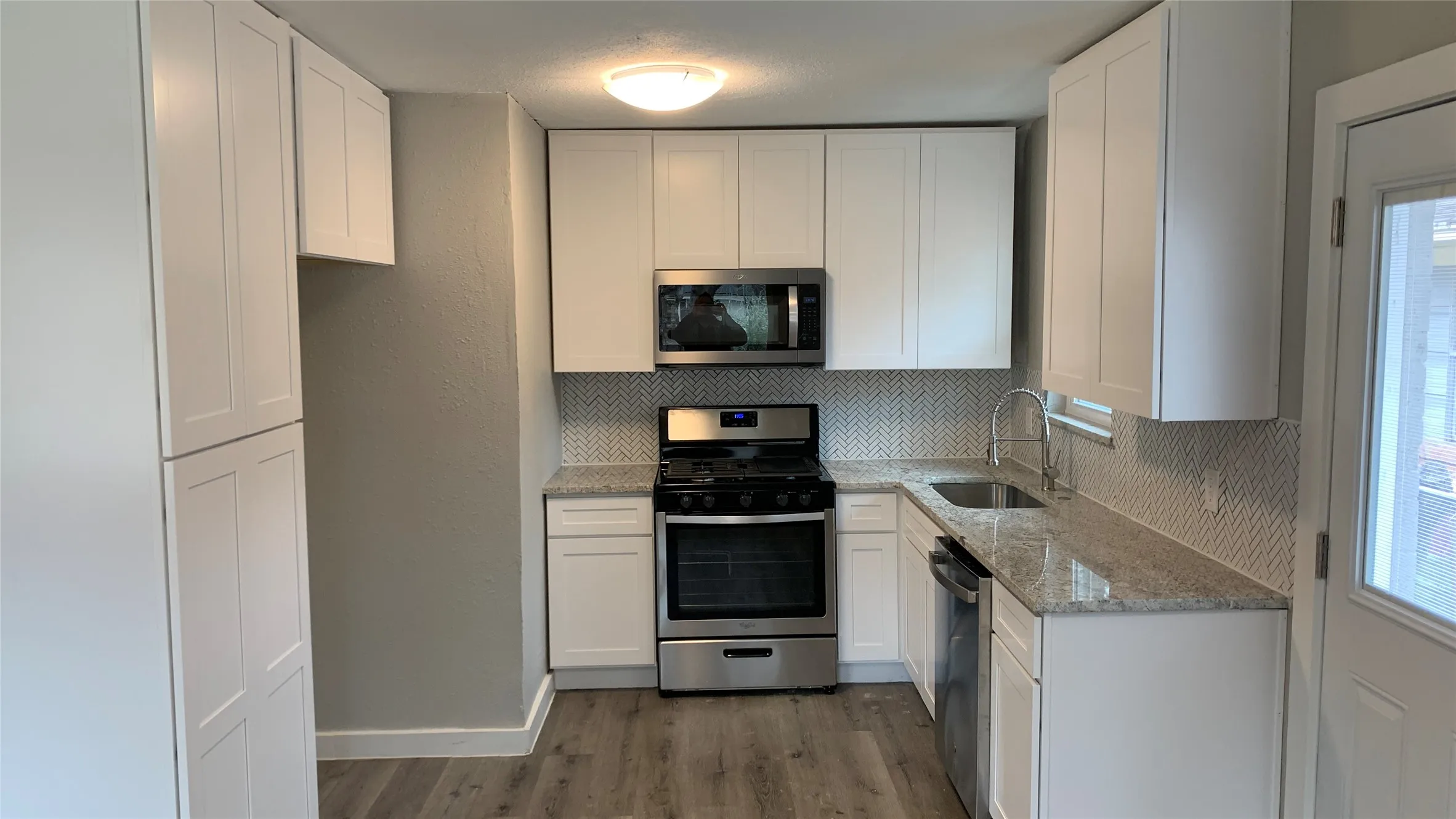 Kitchen featuring white shaker-style cabinetry, stainless steel appliances, granite countertops, and a herringbone tile backsplash