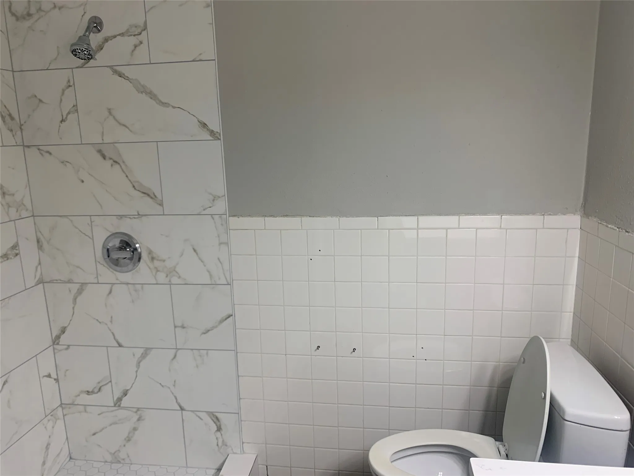 Shower with large format white tile featuring gray veining, chrome showerhead, and matching handle