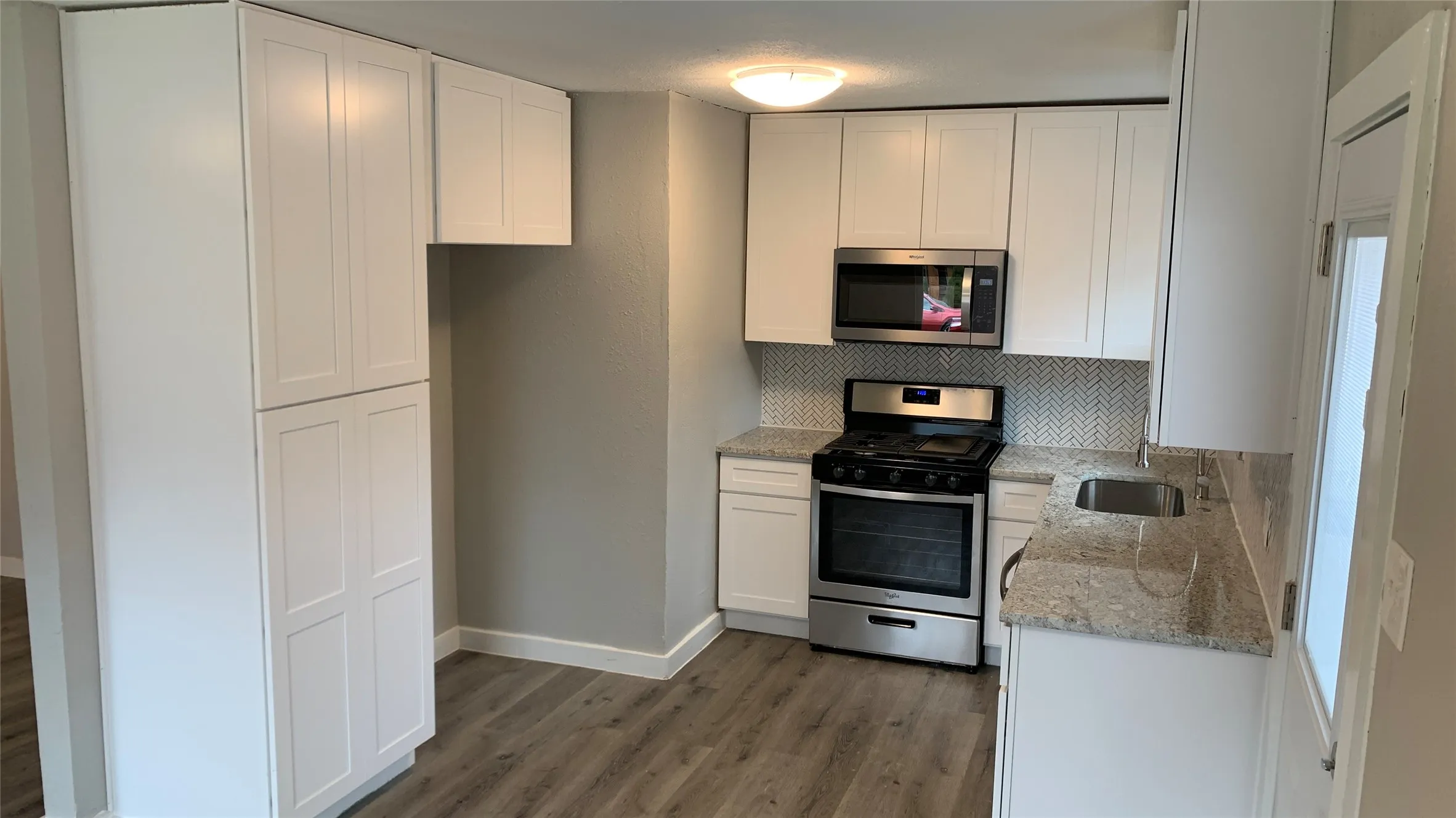Kitchen featuring white shaker-style cabinetry, a stainless steel range with overhead microwave, a stainless steel sink, and light-toned stone countertops