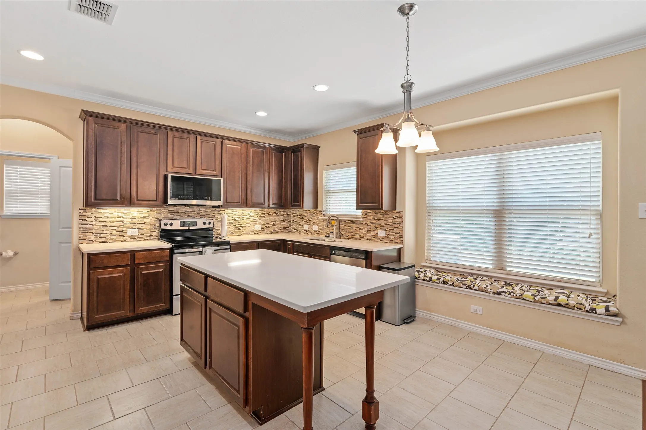 Kitchen featuring dark wood cabinetry, a central island with a solid surface countertop, and a mosaic tile backsplash