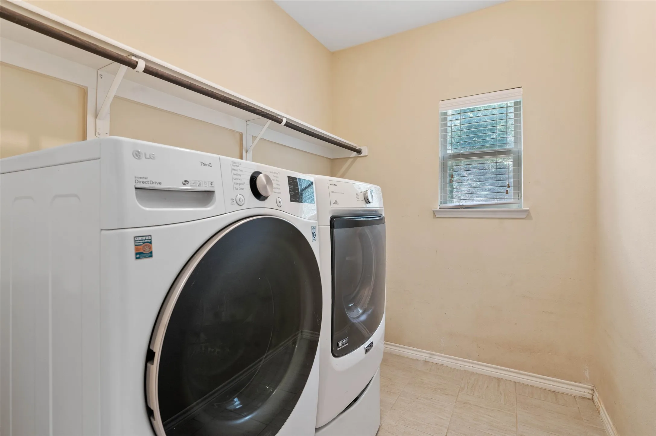 Dedicated laundry space featuring a window, overhead shelving, and light-toned flooring