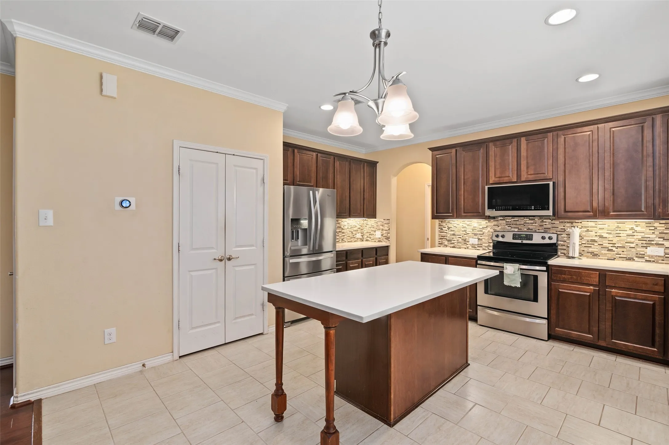 Kitchen featuring a central island with a solid surface countertop, dark wood-finish cabinetry, stainless steel appliances, a mosaic tile backsplash, and recessed lighting