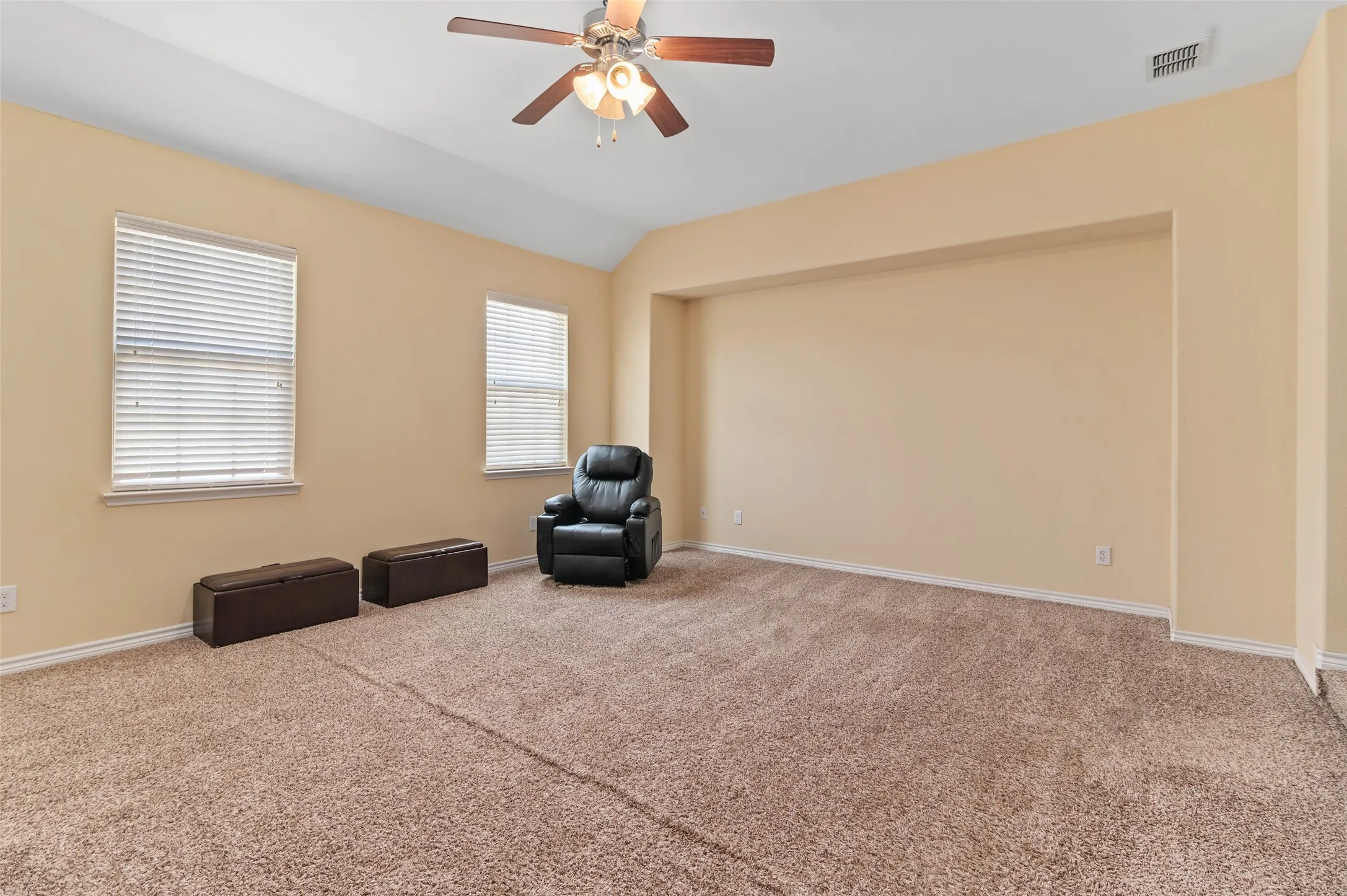 Carpeted room featuring a vaulted ceiling with a fan light fixture, two windows with blinds, and a recessed wall section
