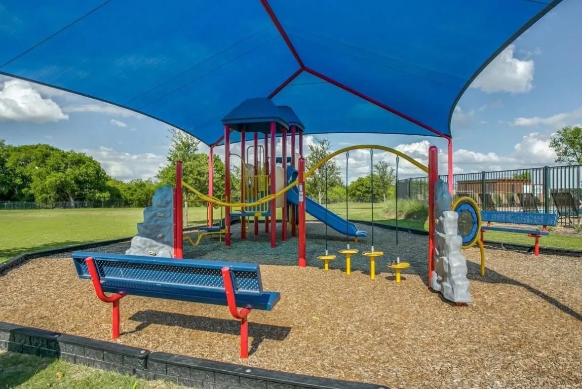 Shaded recreational area featuring a multi-component playground structure with slides and climbing elements
