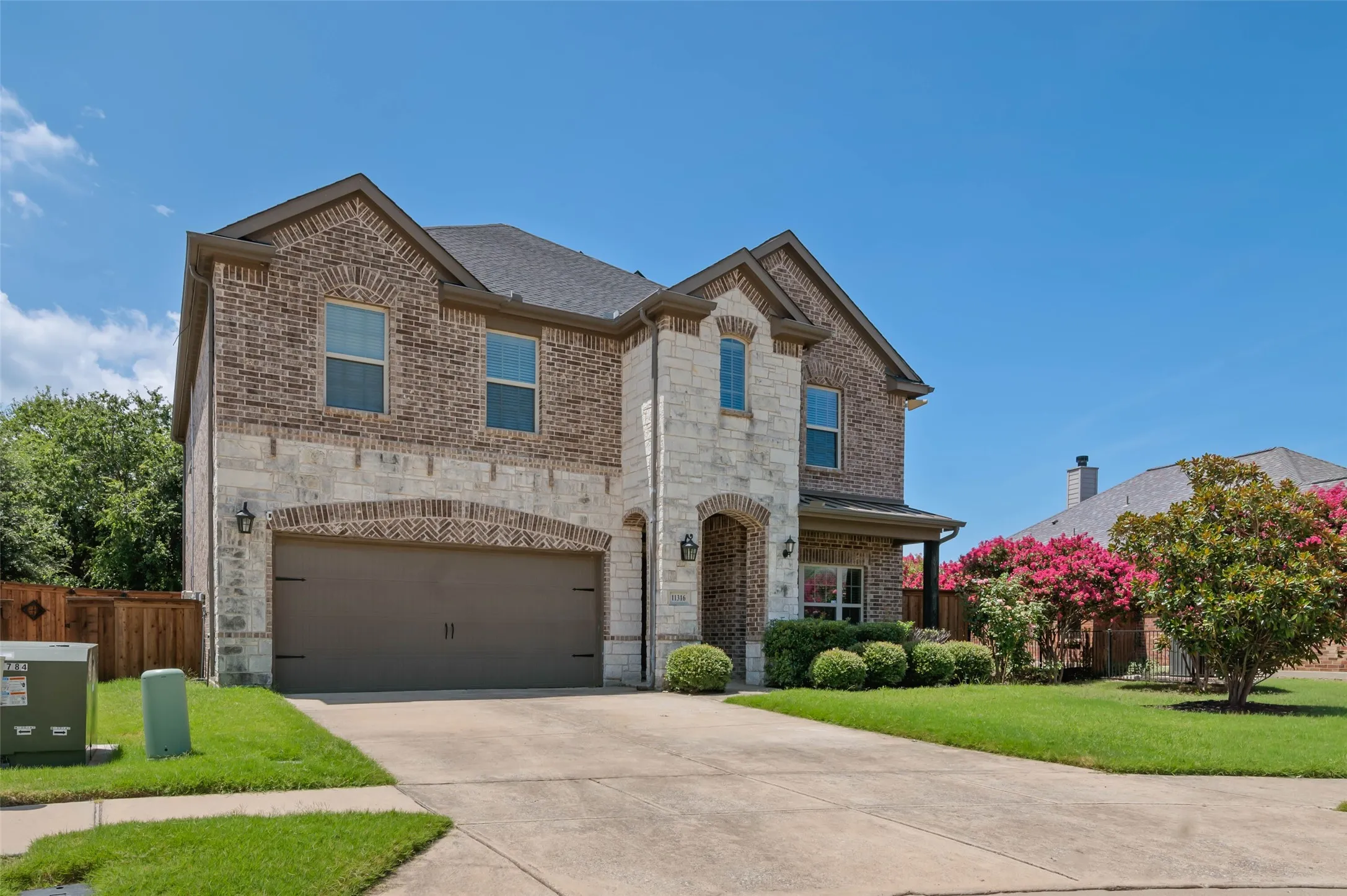 Two-story brick and stone facade residence featuring an arched entry, a two-car garage with an arched brick accent, and mature landscaping