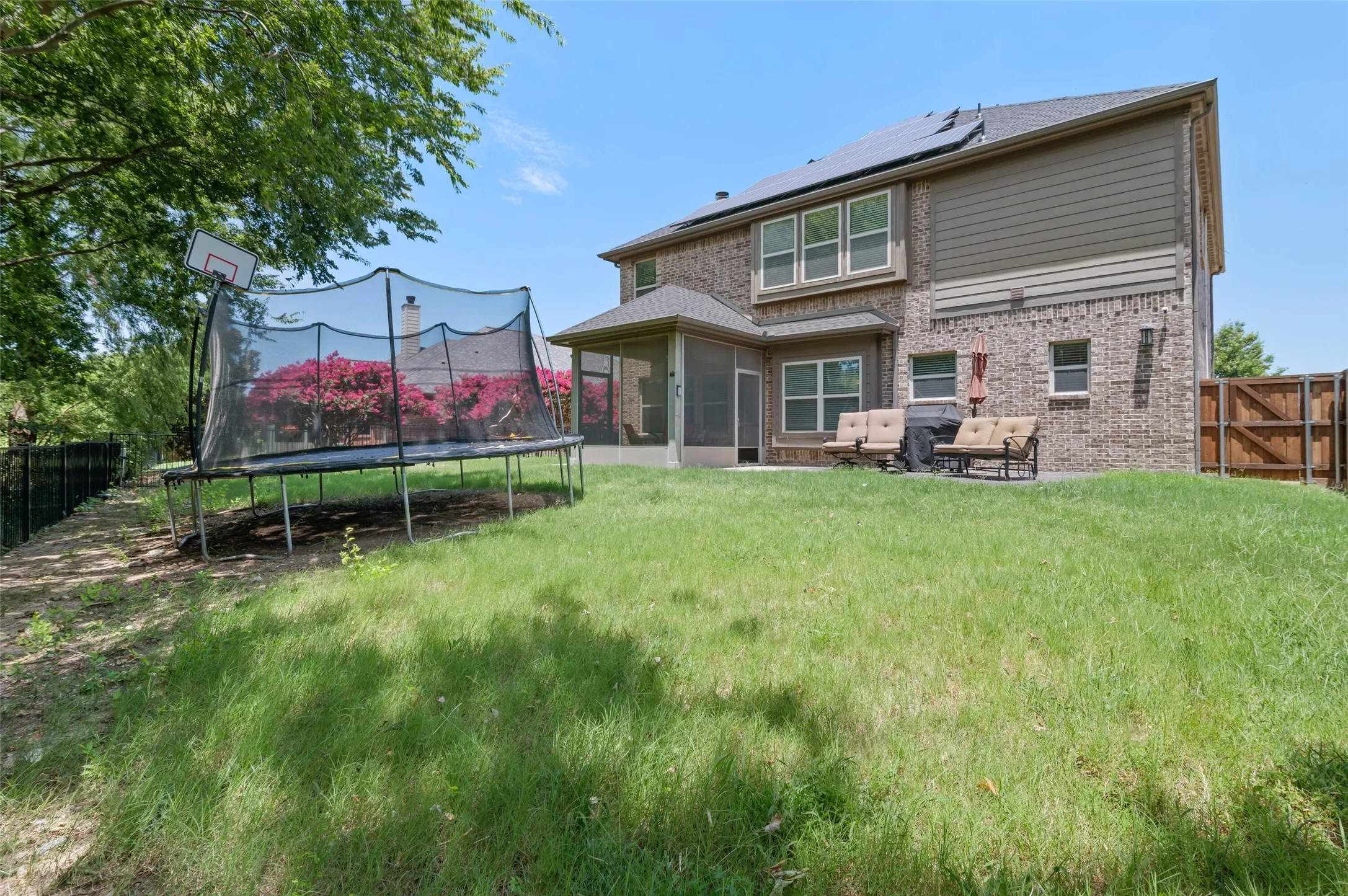 Expansive backyard with a manicured lawn, brick exterior, screened patio, upper-level windows, and a privacy fence