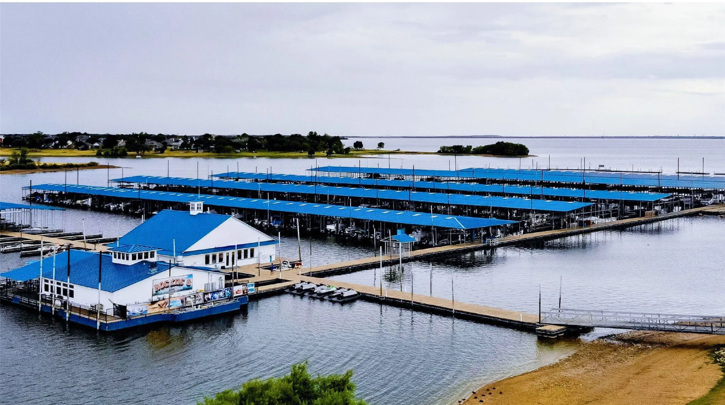 Expansive marina with numerous covered boat slips, a large floating building with a blue roof, and multiple dock structures