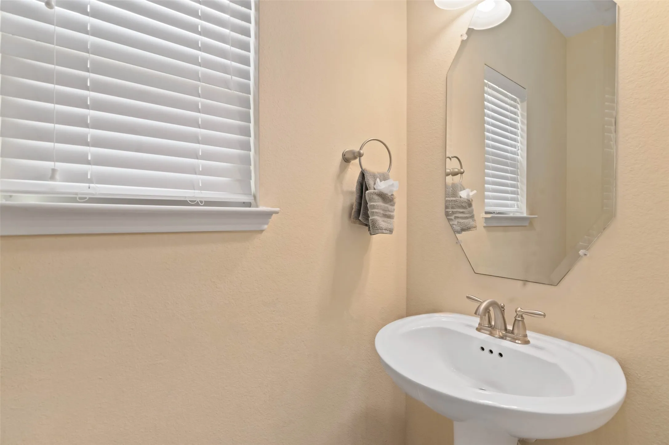 Pedestal sink with brushed nickel faucet, an octagonal mirror, and a window with horizontal blinds
