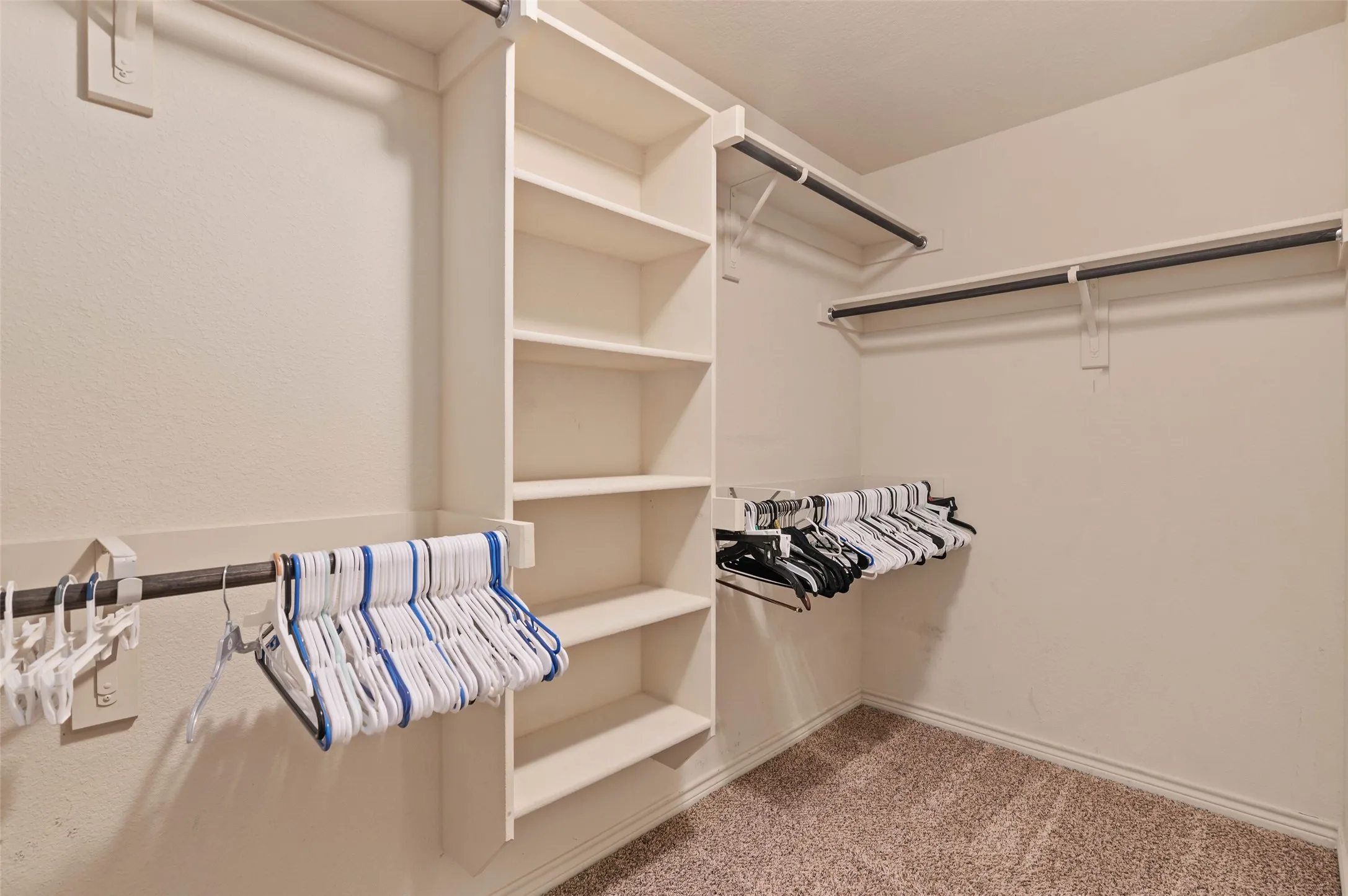 Walk-in closet featuring built-in shelving, multiple hanging rods, and neutral-toned carpeting