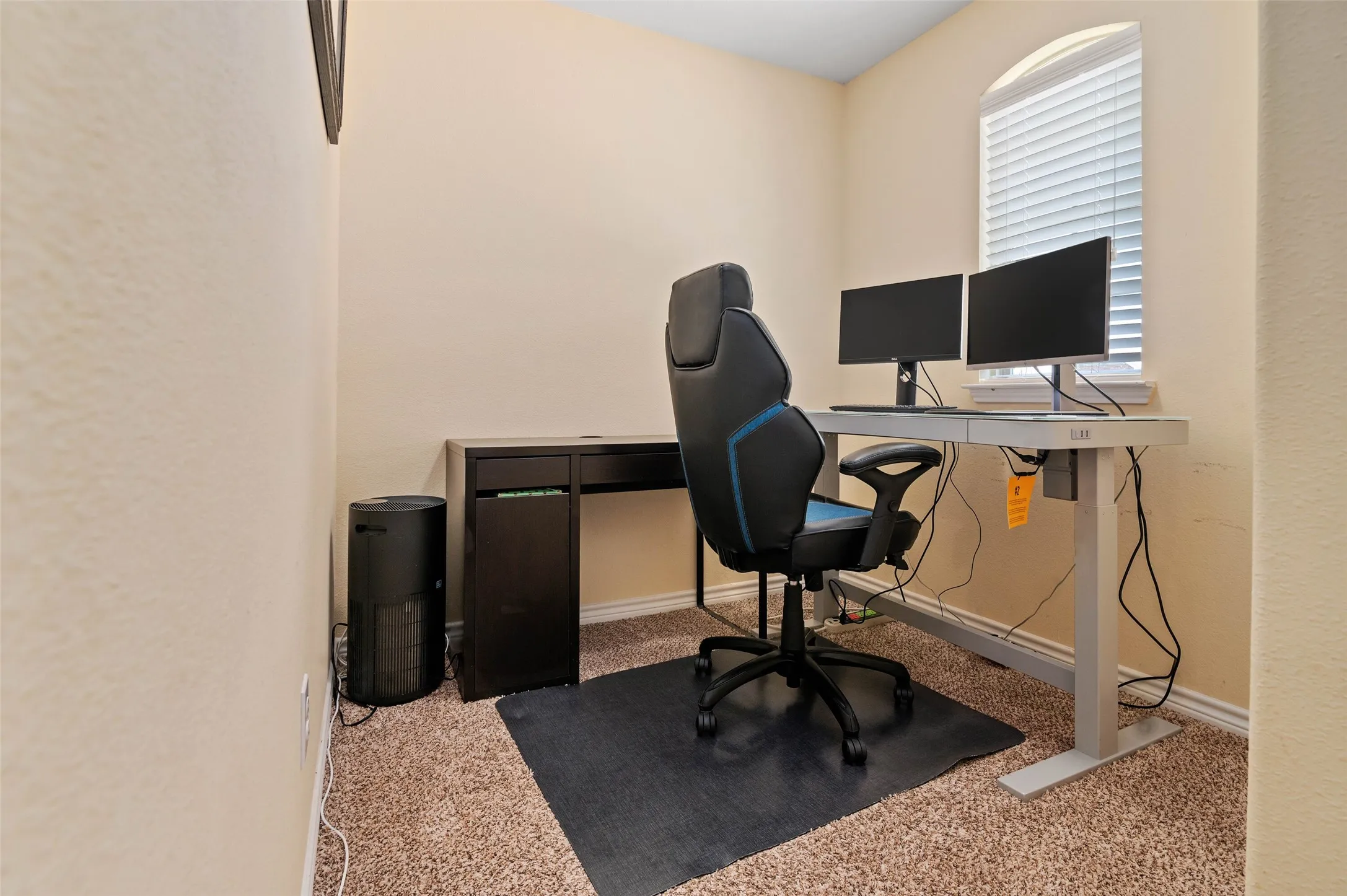 Carpeted room featuring an arched window with horizontal blinds, light-toned walls, and a built-in baseboard