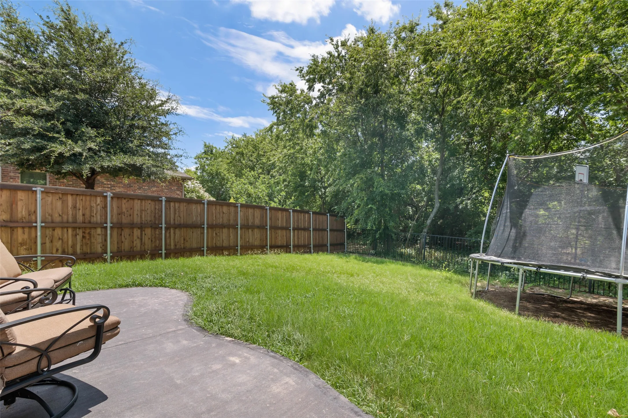 Expansive backyard featuring a concrete patio, a manicured lawn, a privacy fence, and mature trees providing natural shading