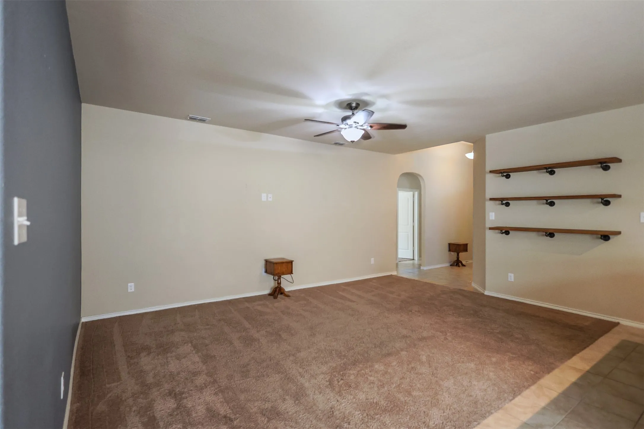Carpeted living area featuring a ceiling fan with light fixture, built-in wall shelving, and an arched doorway
