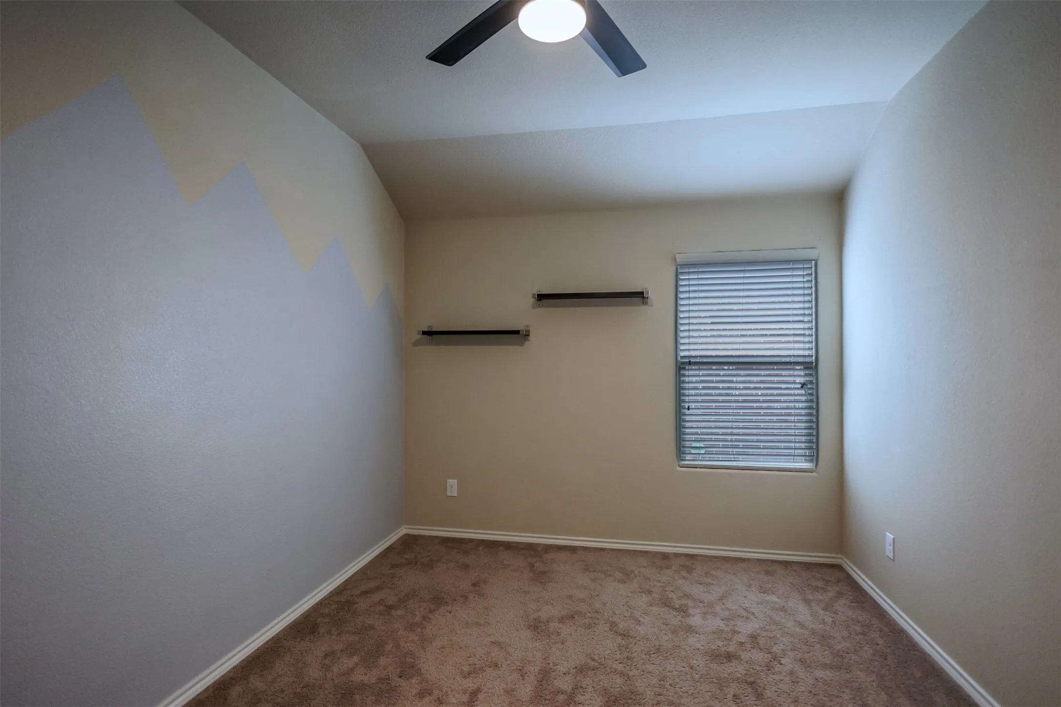Carpeted room featuring a ceiling fan with integrated lighting, a window with blinds, and two wall-mounted shelves