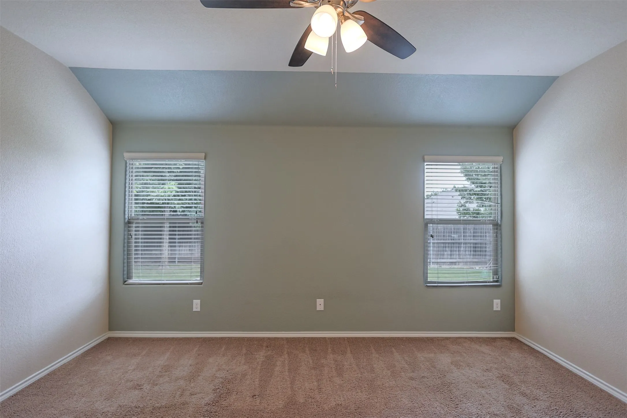 Recessed ceiling with an accent color, neutral wall tones, two windows with blinds, and a ceiling fan with light fixture