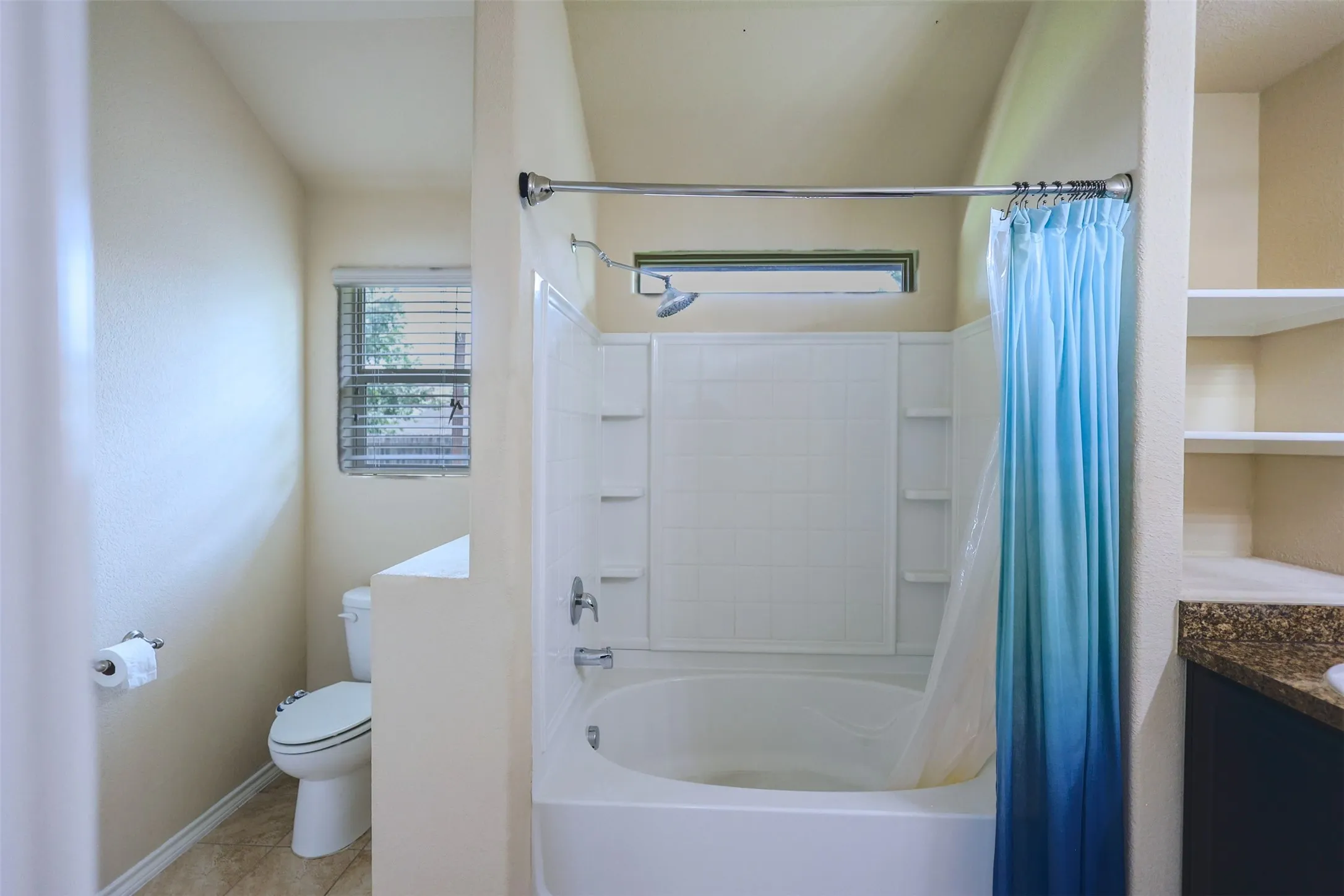 Full bathroom featuring a tub/shower combination with white subway tile surround, a built-in shelf system, and a vanity with a stone-finish countertop