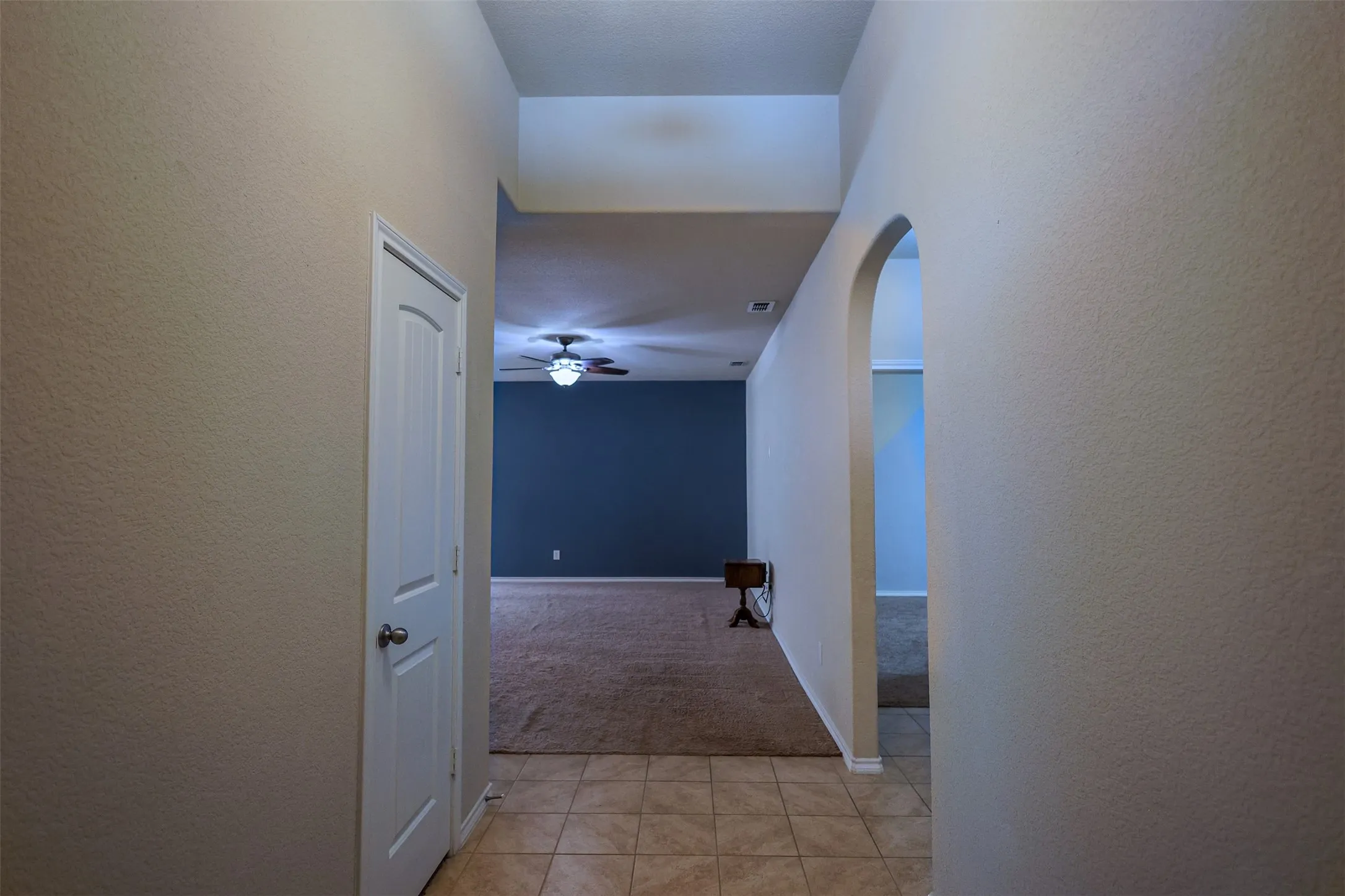 Hallway featuring tile flooring, a white interior door, and a decorative arched entryway