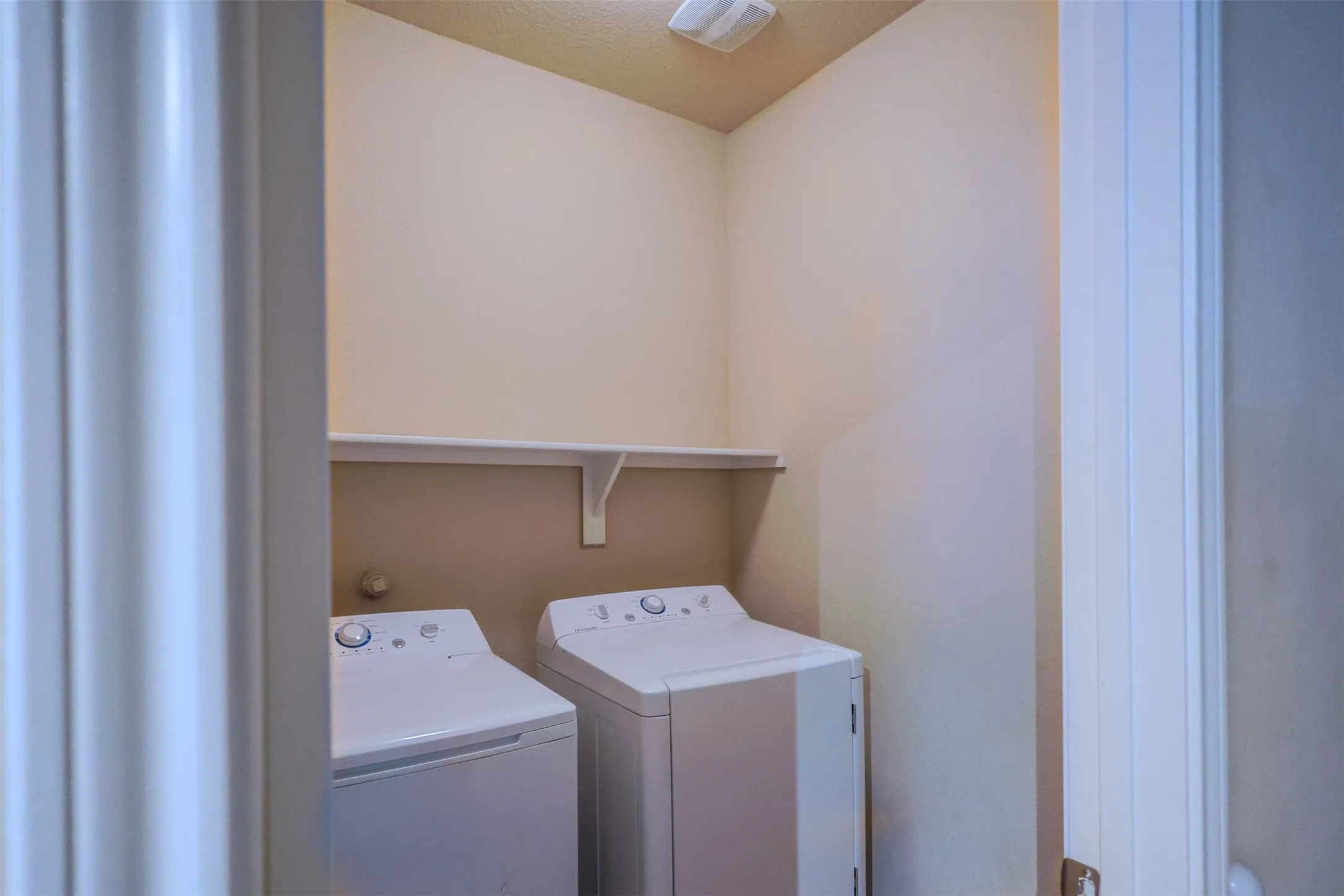 Laundry area with an upper storage shelf and neutral wall tones