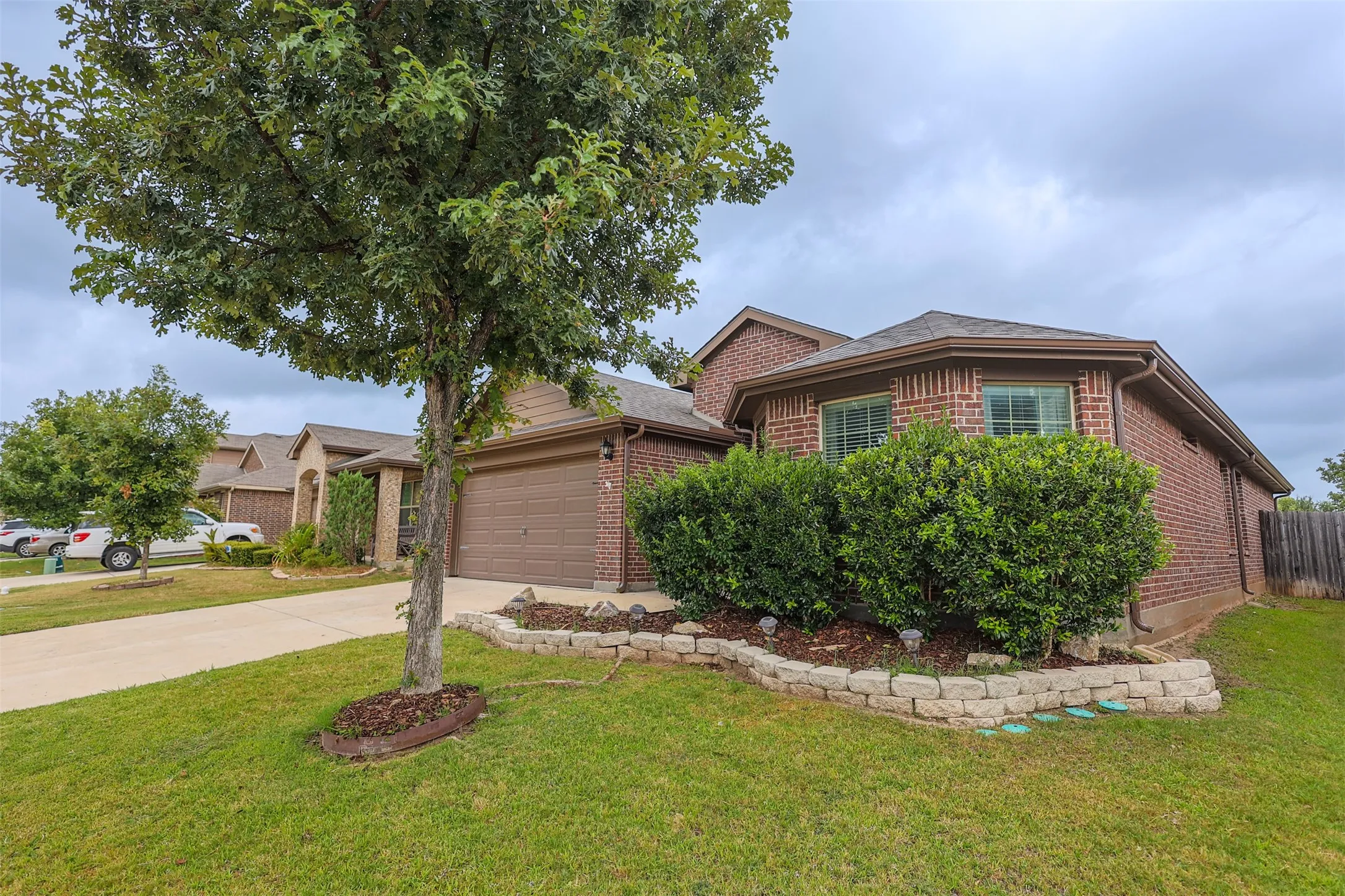 Brick exterior with a brown shingled roof, featuring a two-car garage and mature landscaping