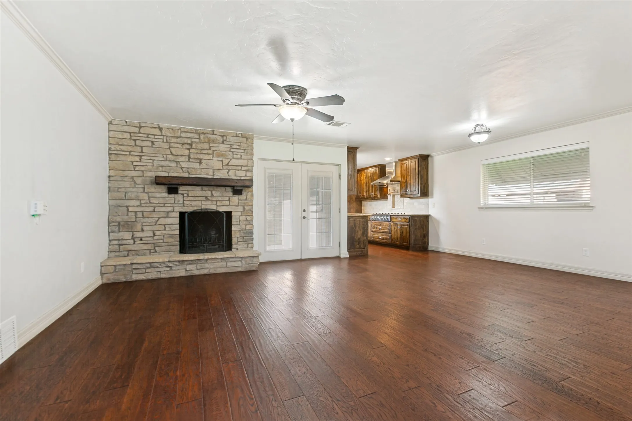 Open plan living room with fireplace and French doors to backyard and paved patio area