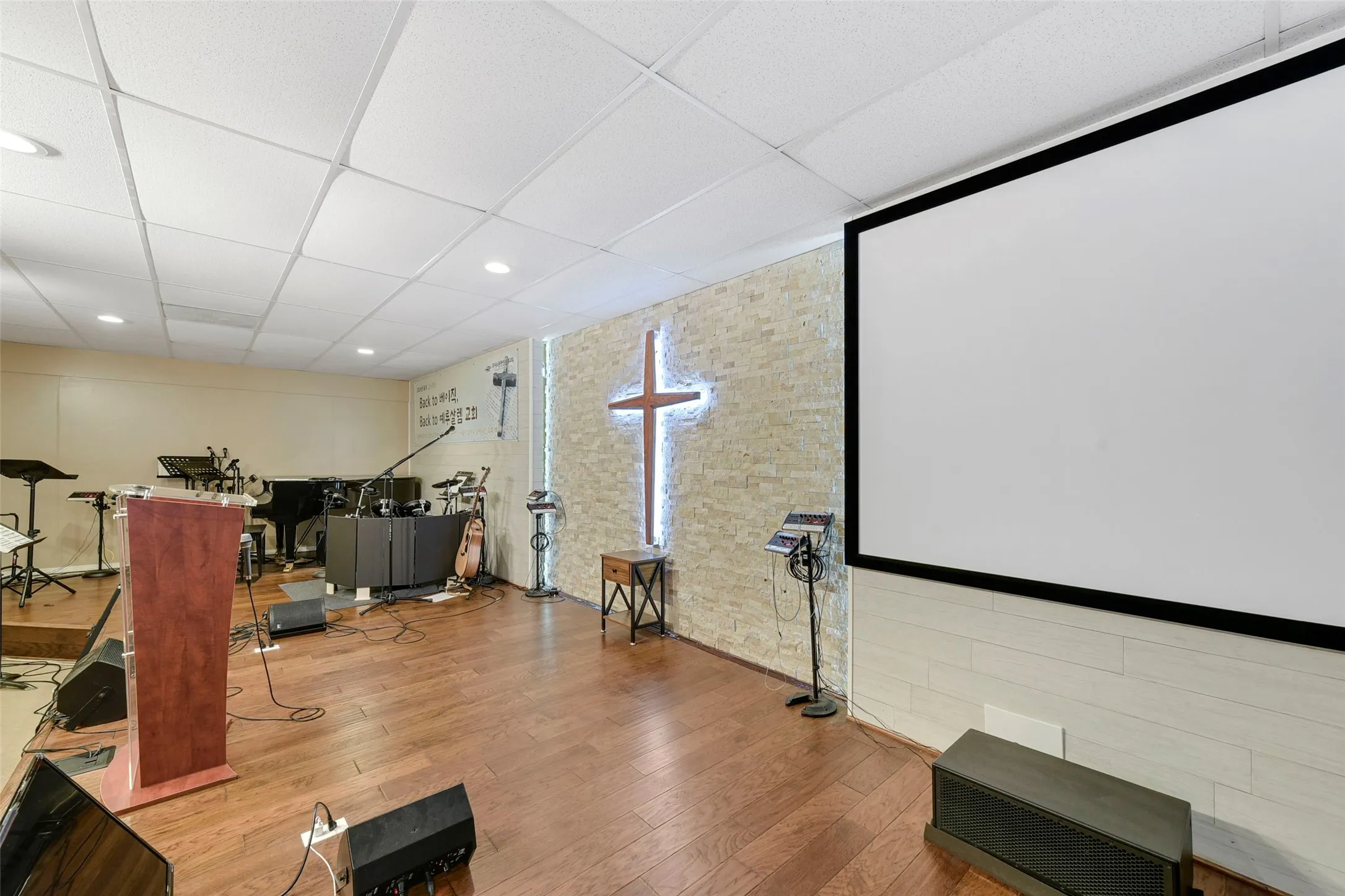 Spacious interior featuring wood-finish flooring, a large projection screen, and a textured wall with architectural lighting