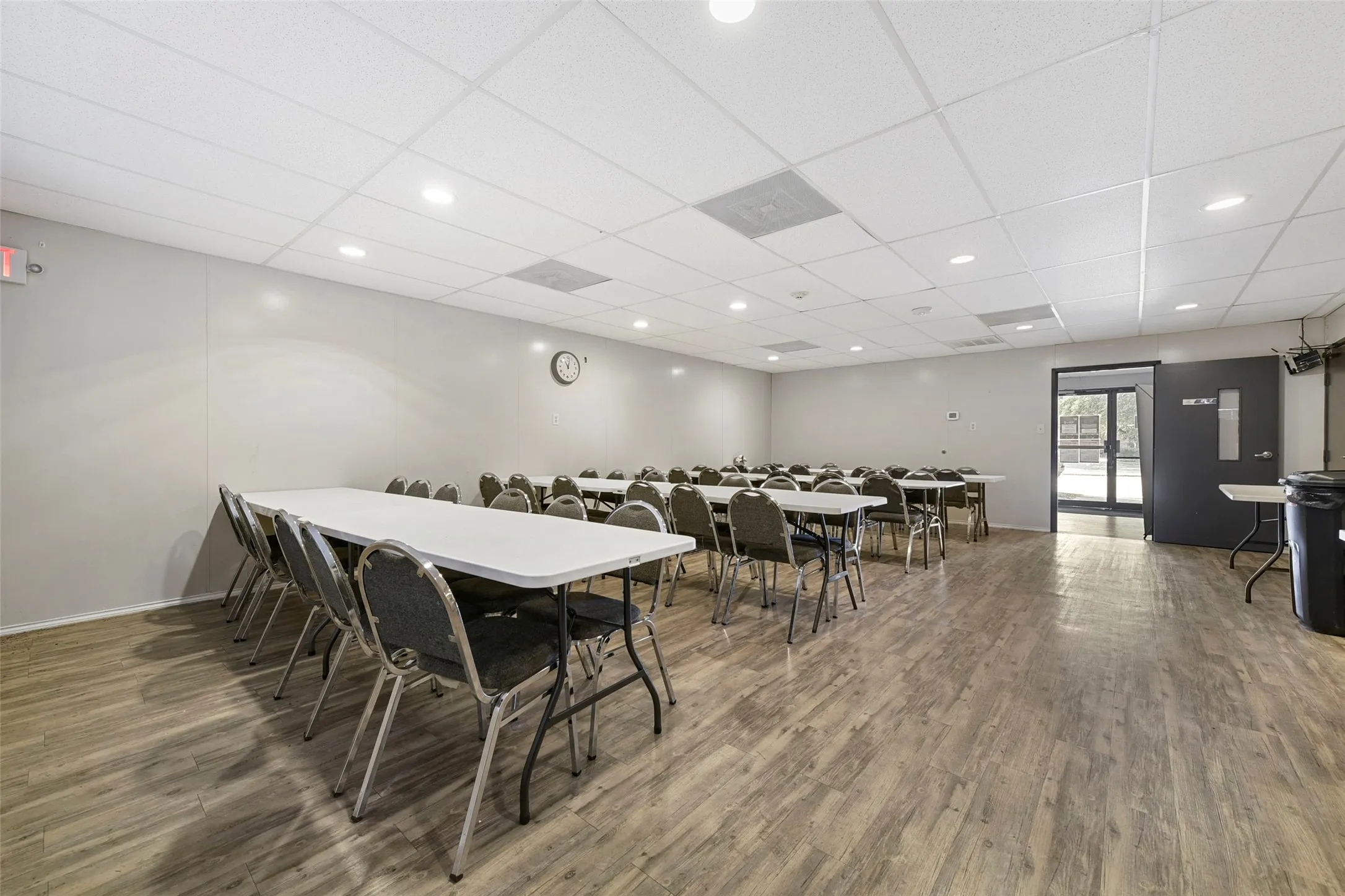 Spacious interior room with wood-finish flooring, drop ceiling with recessed lighting, and light gray walls