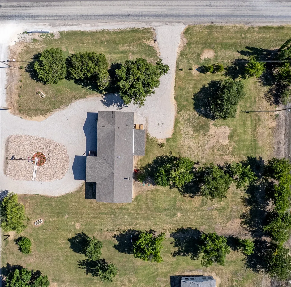 Expansive property featuring a grey-pitched roof structure, surrounded by a gravel driveway and green landscaping