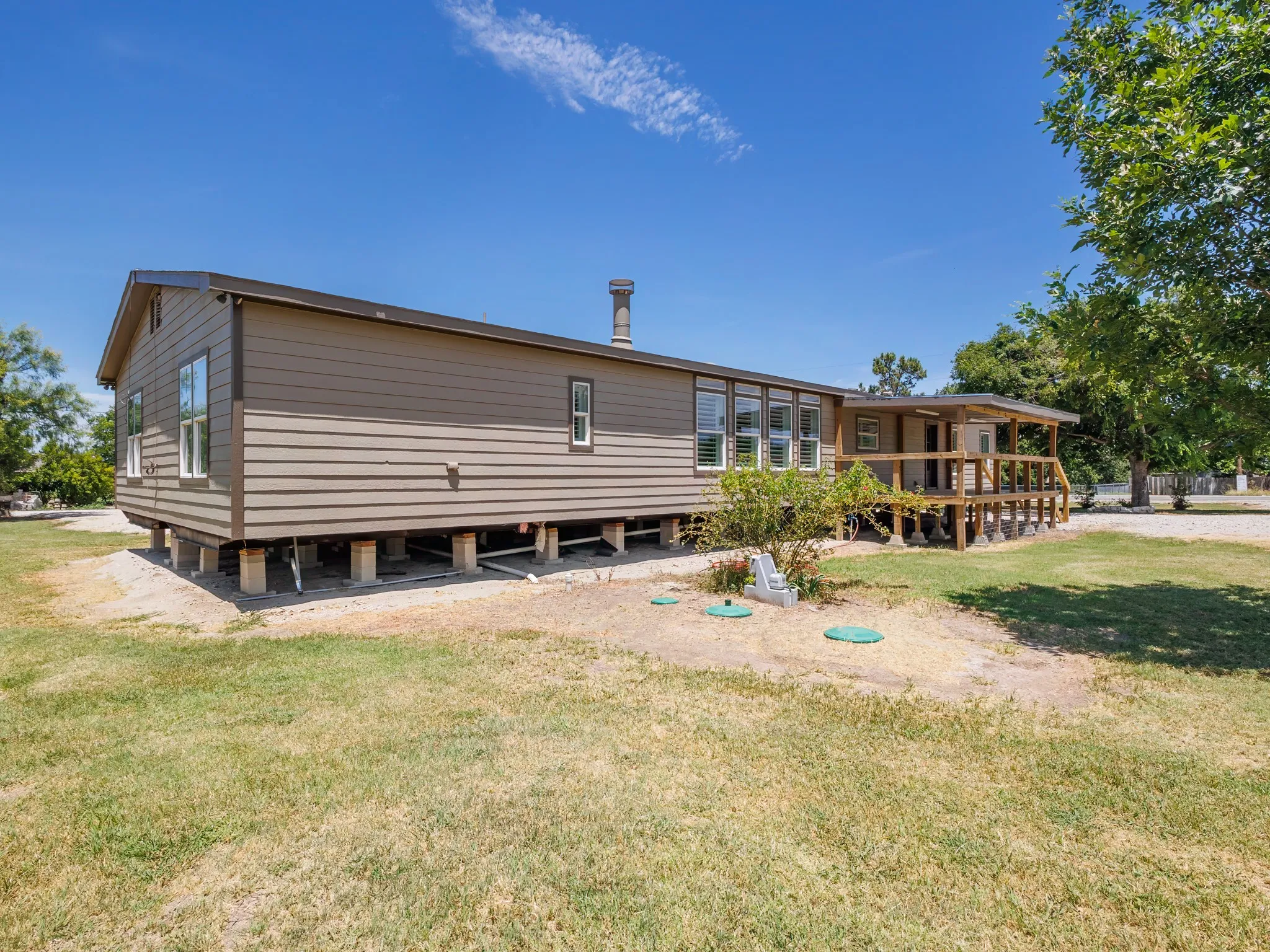 Single-story property with horizontal siding, multiple window configurations, an elevated covered porch with wood decking and railings, and a prominent chimney feature