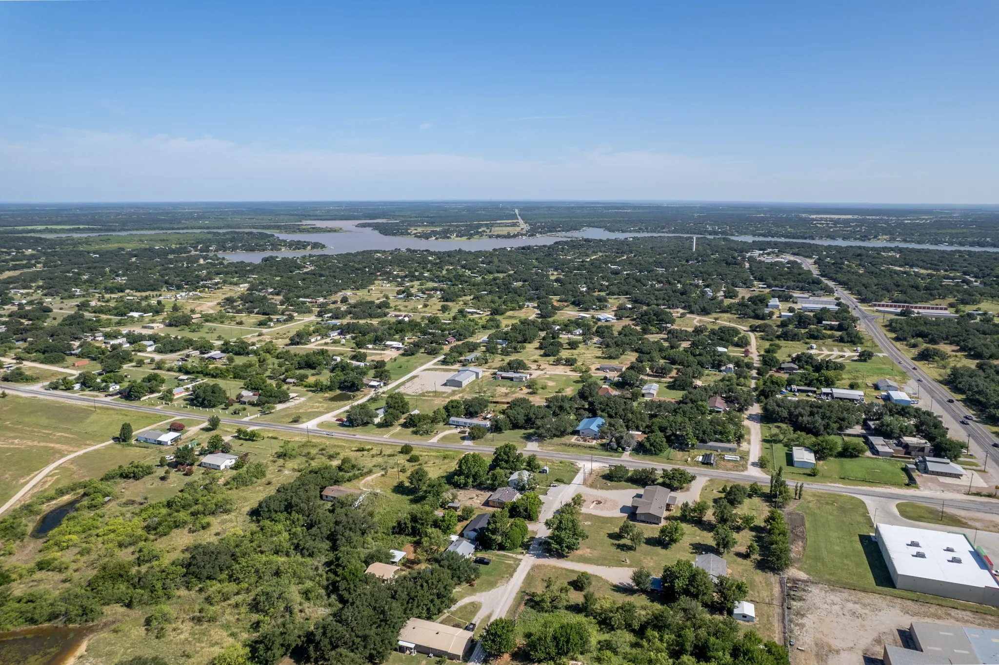 Aerial perspective showcasing a residential area with varied housing structures, extensive tree cover, and a distant body of water
