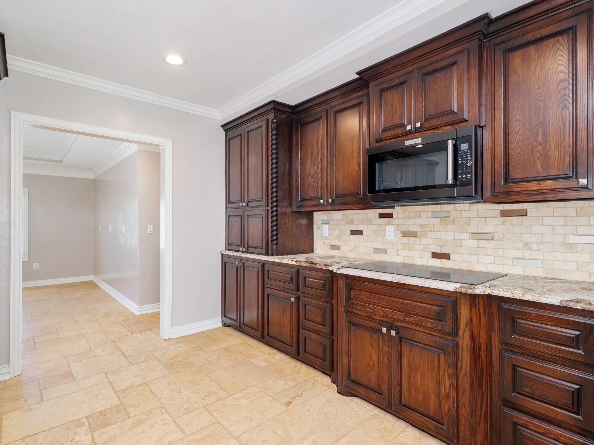 Kitchen featuring dark wood cabinetry, a built-in microwave, a black cooktop, light-toned stone countertops, and a subway tile backsplash