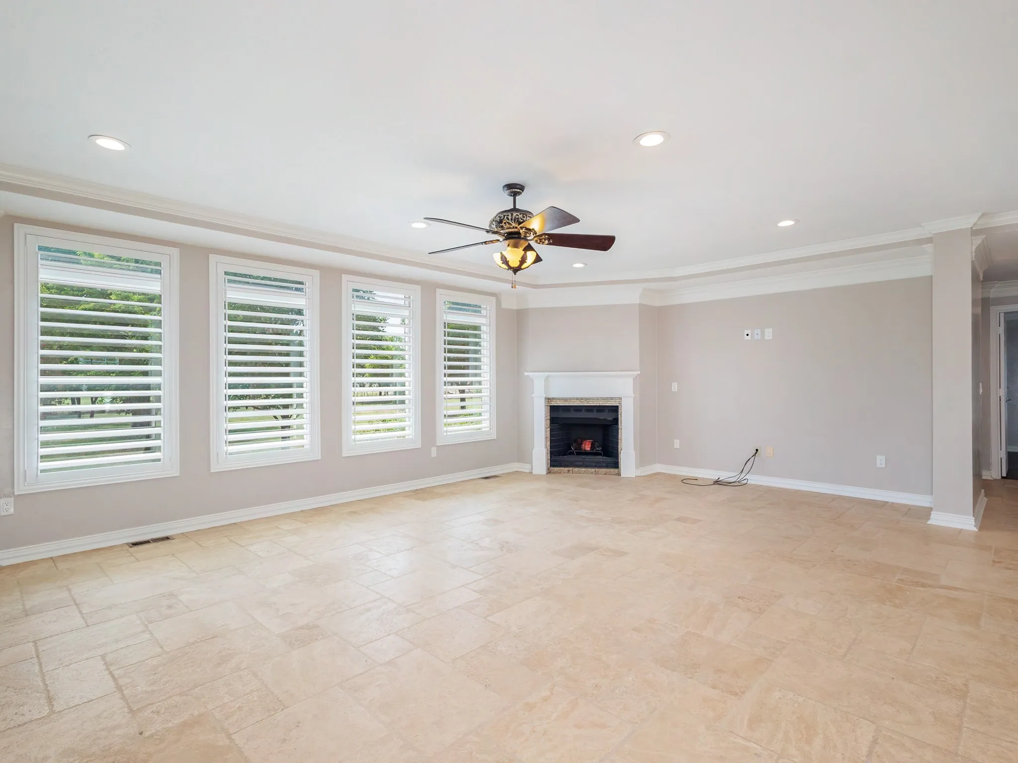Spacious room featuring light-toned tile flooring, a fireplace with a white mantel, and four large windows with white louvered shutters