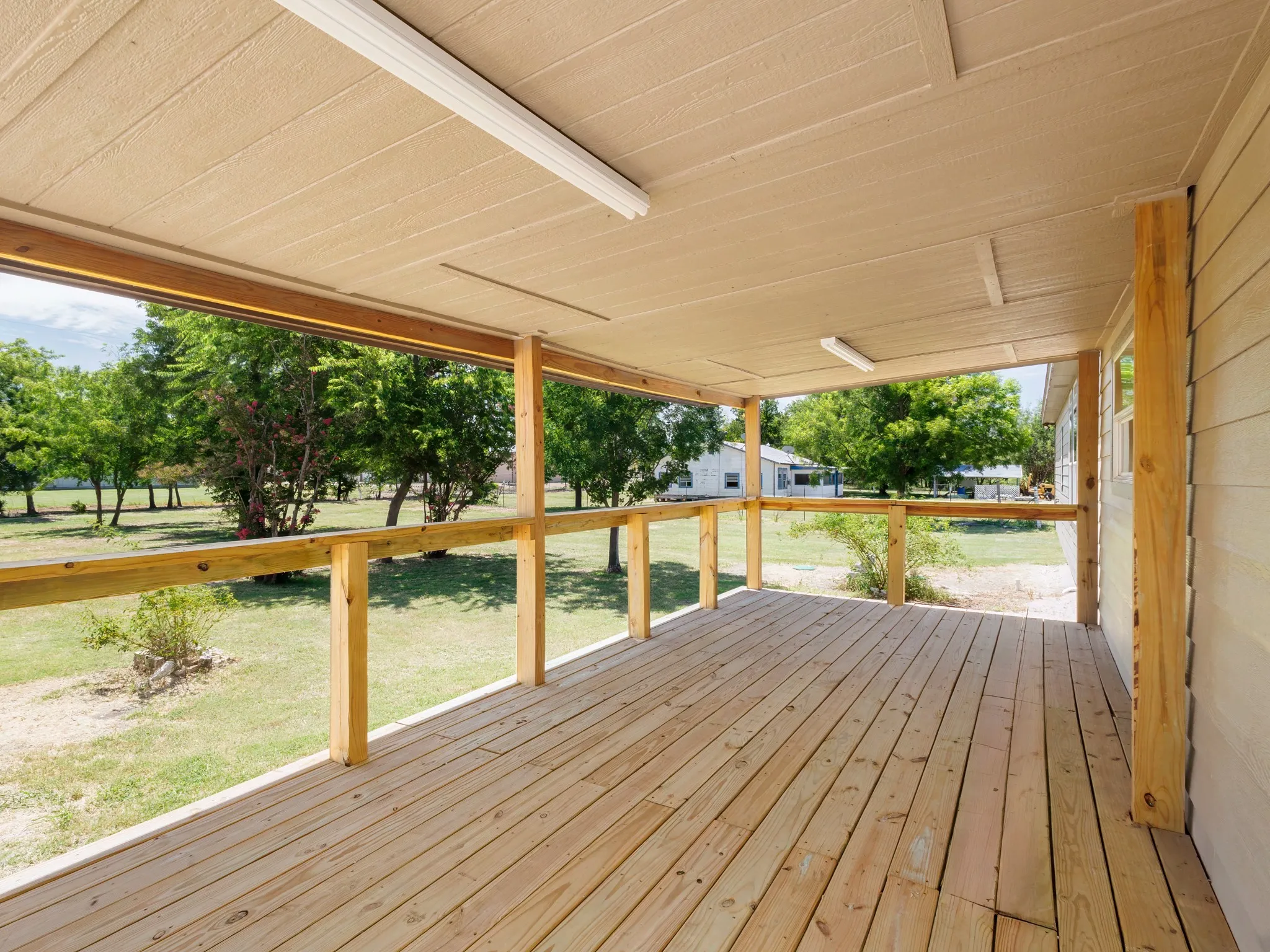 Covered wooden deck featuring a wooden railing, overhead lighting fixtures, and a textured ceiling