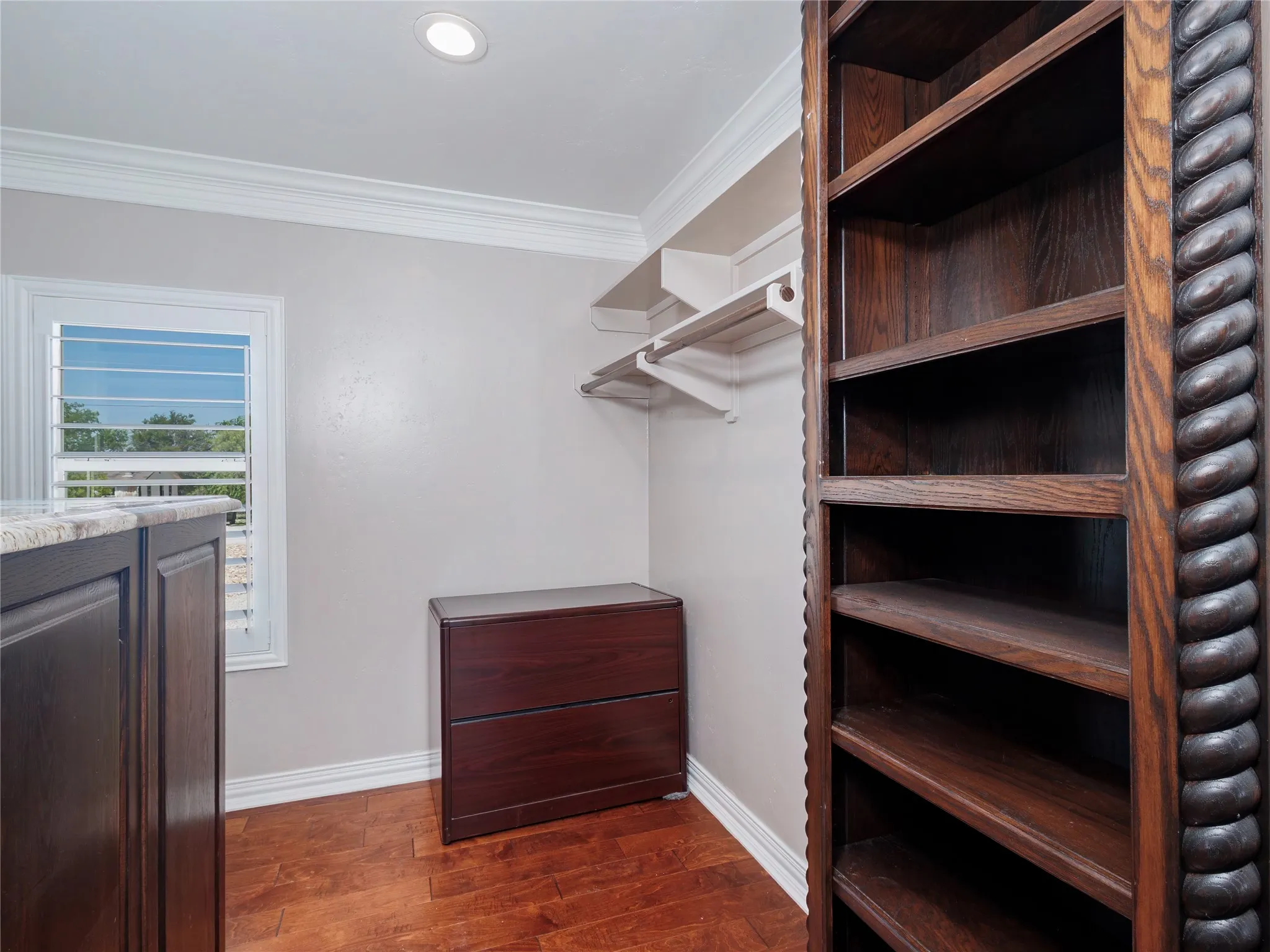 Walk-in closet featuring wood-finish flooring, built-in shelving, adjustable hanging rods, a window with plantation shutters, and recessed lighting