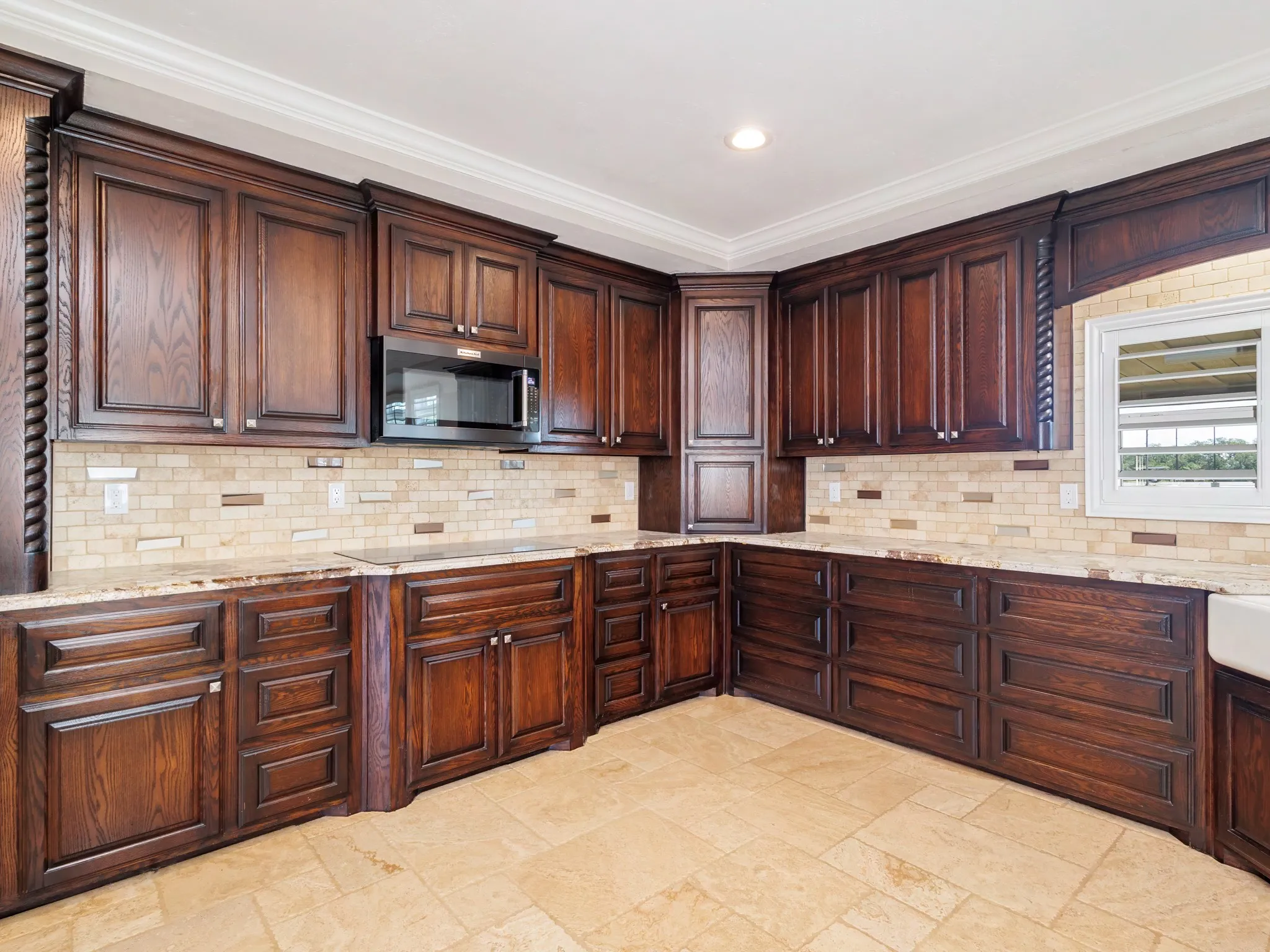 Kitchen featuring rich wood cabinetry, light-toned stone countertops, a tile backsplash with decorative accents, a built-in microwave, and ceramic tile flooring