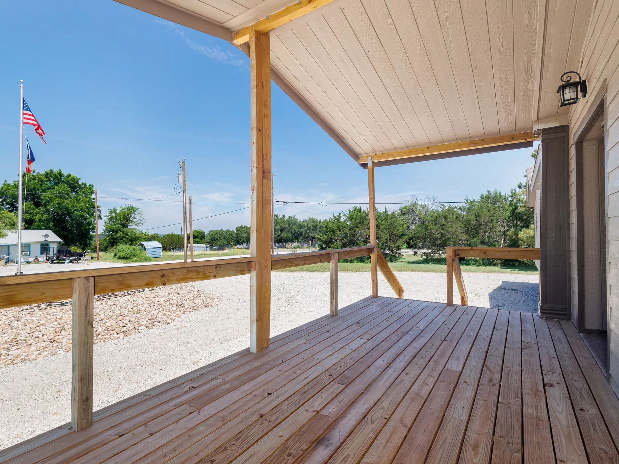 Spacious covered porch with natural wood decking and railings, featuring exposed wood support beams, a light-toned soffit, and an exterior wall light fixture