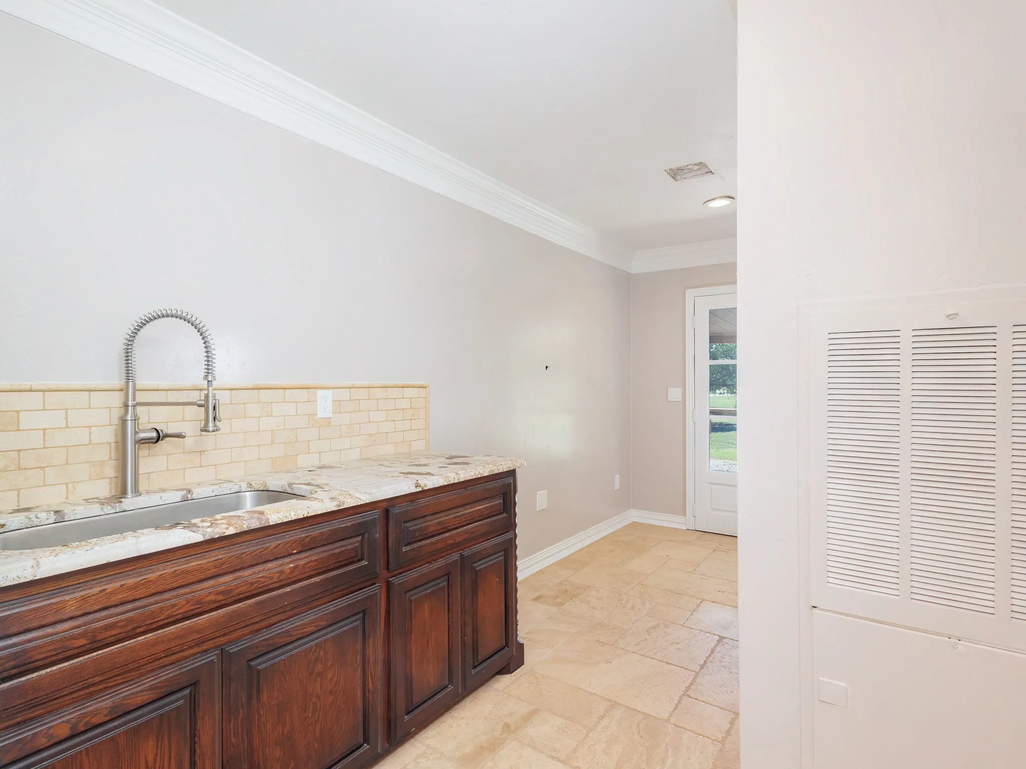Utility sink area featuring wood cabinetry, a light-toned tile backsplash, and a granite-style countertop