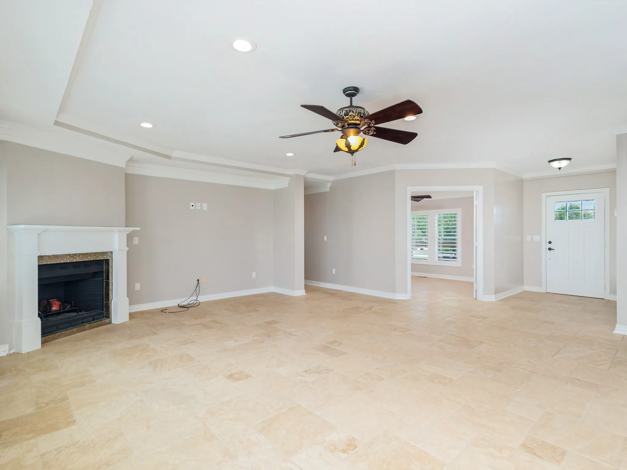 Spacious interior featuring light-toned tile flooring, a fireplace with a white mantel and granite surround, and a tray ceiling