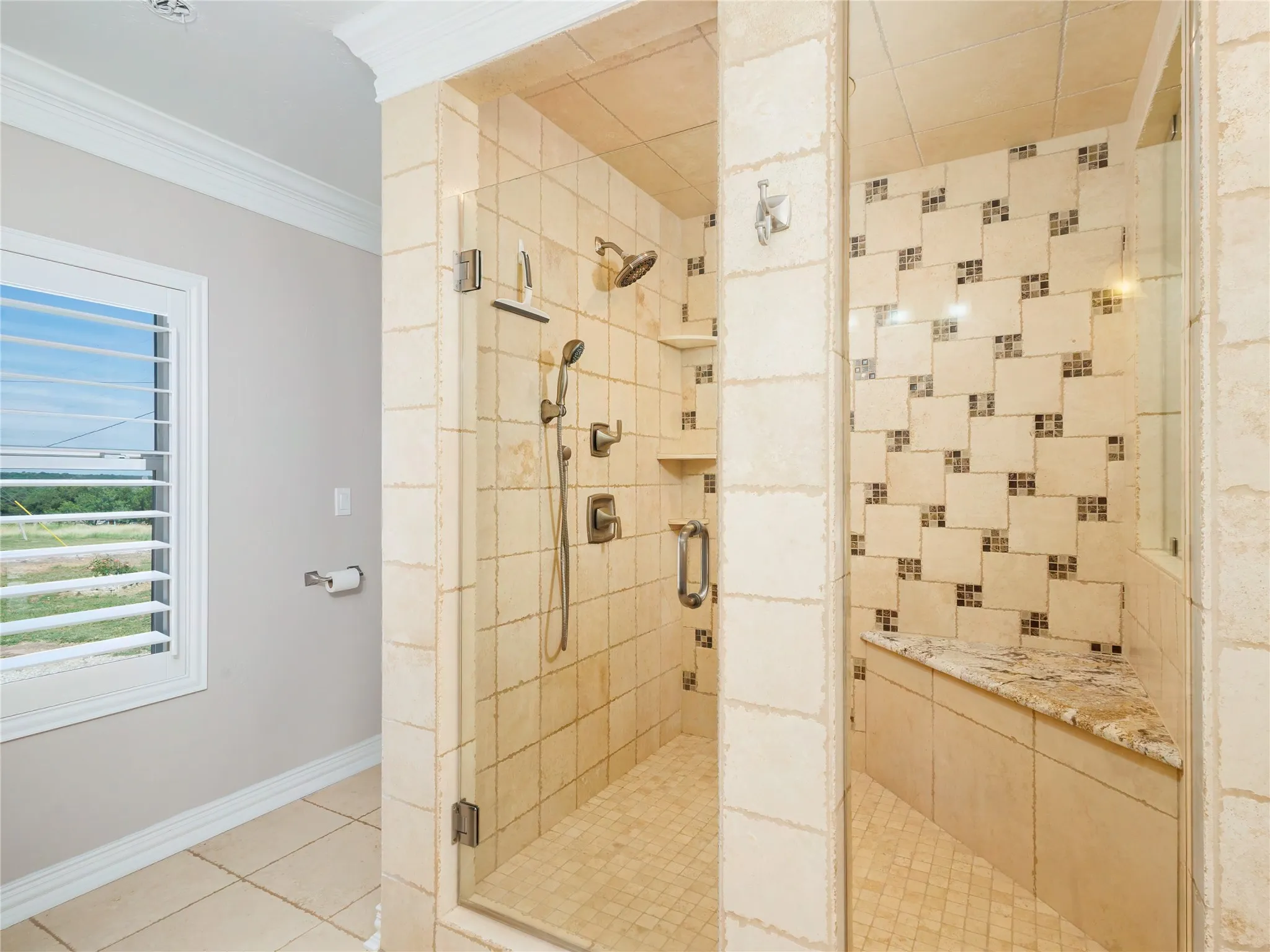 Walk-in shower with clear glass enclosure, multiple shower heads, and an integrated bench with a natural stone top