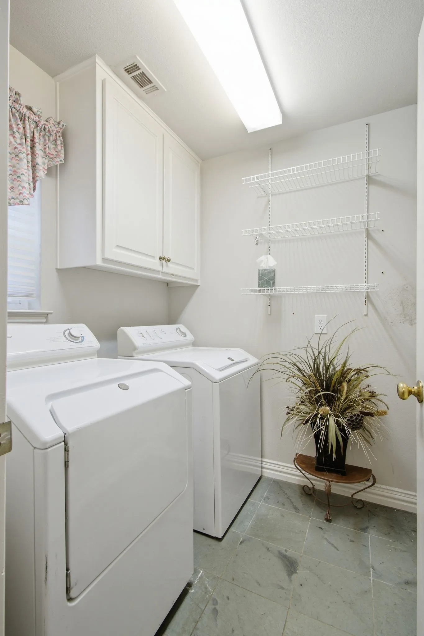 Dedicated laundry area featuring a tiled floor, overhead cabinetry, and wall-mounted shelving