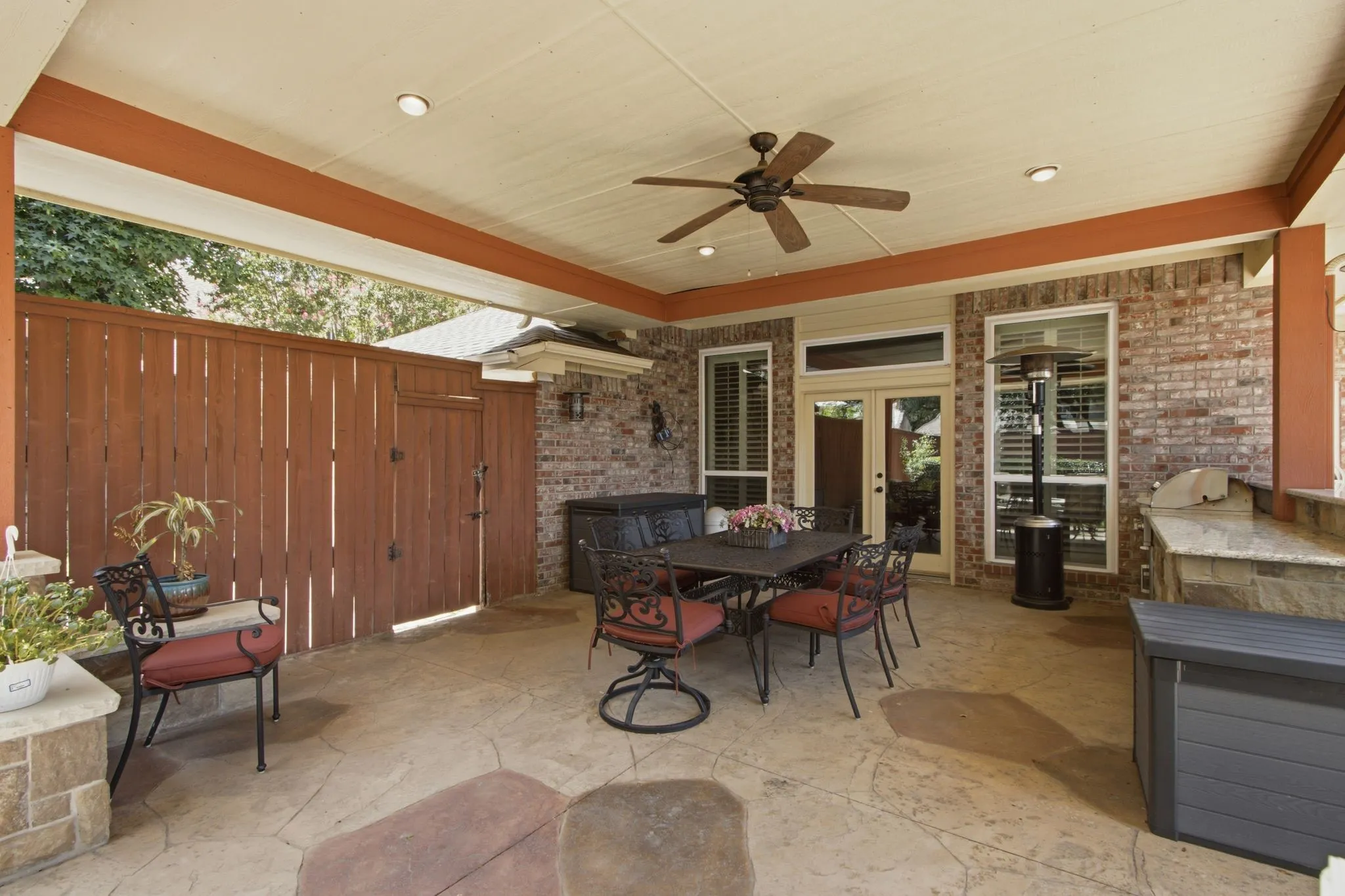 Covered outdoor patio featuring stamped concrete flooring, brick exterior, and a built-in outdoor kitchen with stone veneer and a light-toned countertop